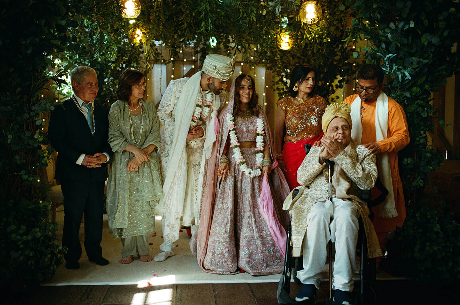 Bride and groom stand with family beneath glowing lights during intimate wedding ceremony.