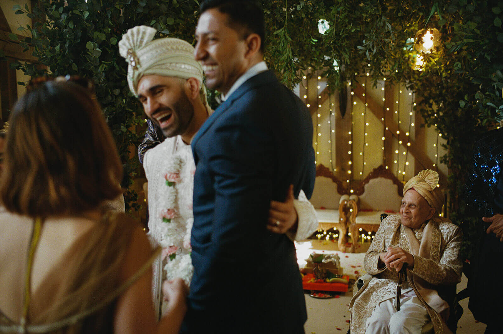 Guests laugh together during a joyful Indian wedding ceremony beneath twinkling lights.