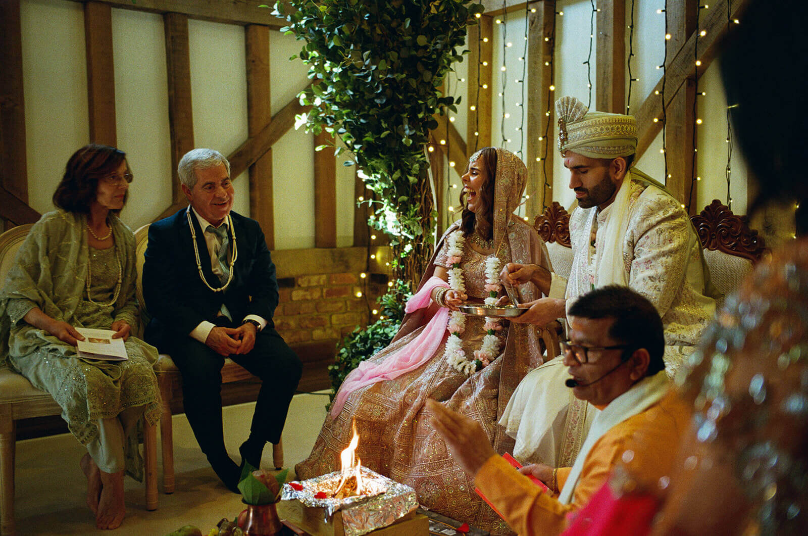 Bride laughing during Hindu wedding ceremony as groom holds ritual tray beside sacred fire
