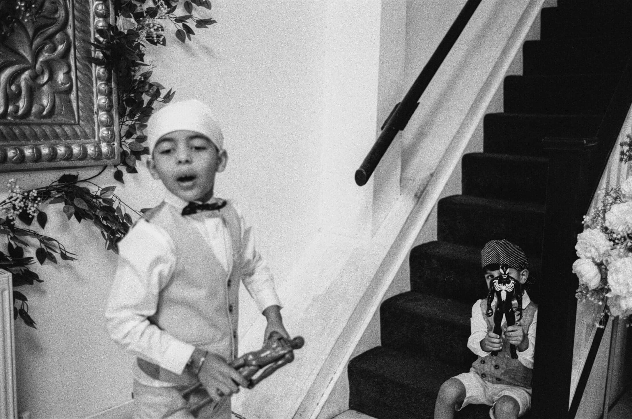 Black and white analogue photograph of a young boy in a turban standing beside a staircase