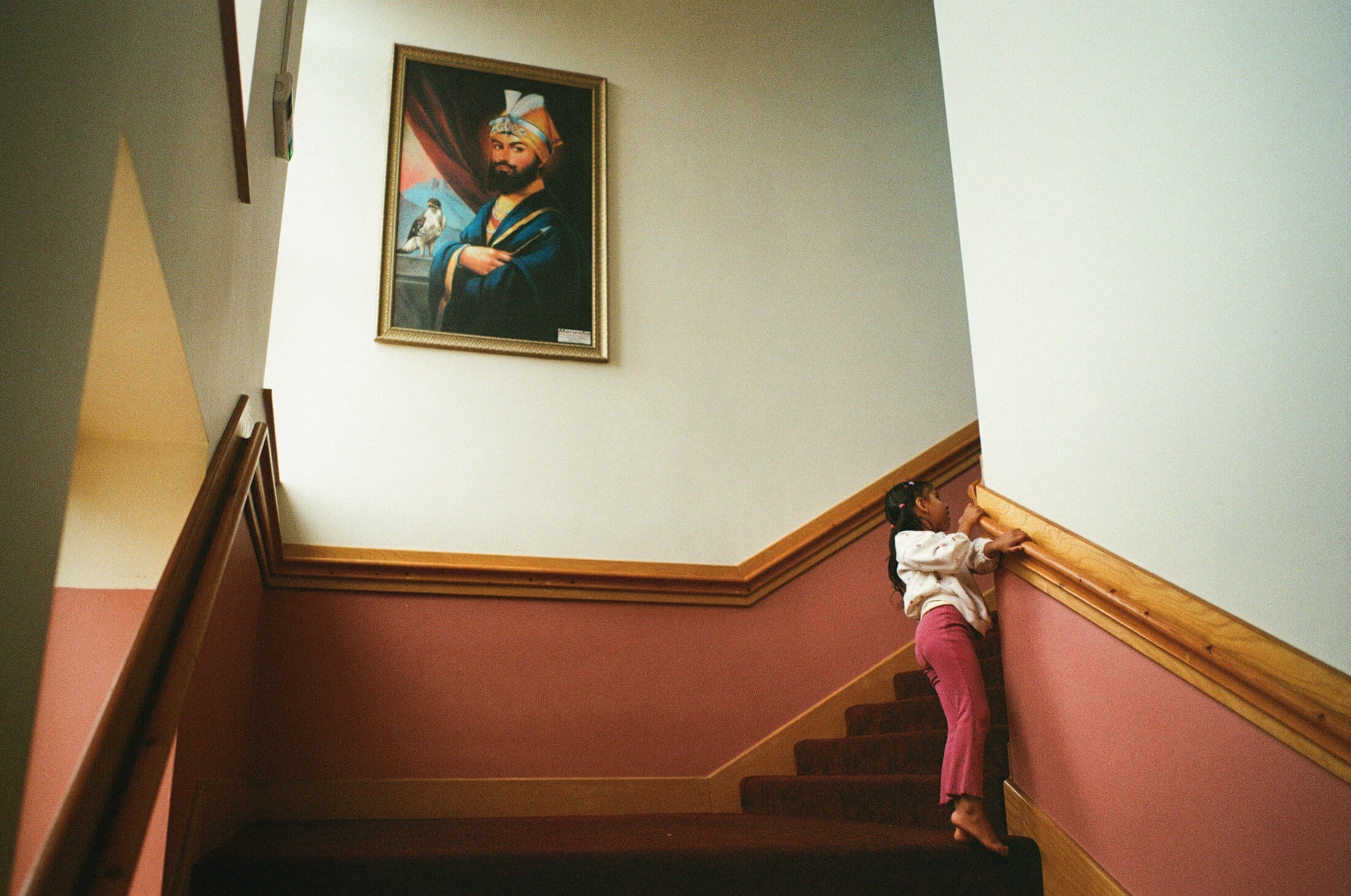 Child peeking around a staircase beneath a framed portrait