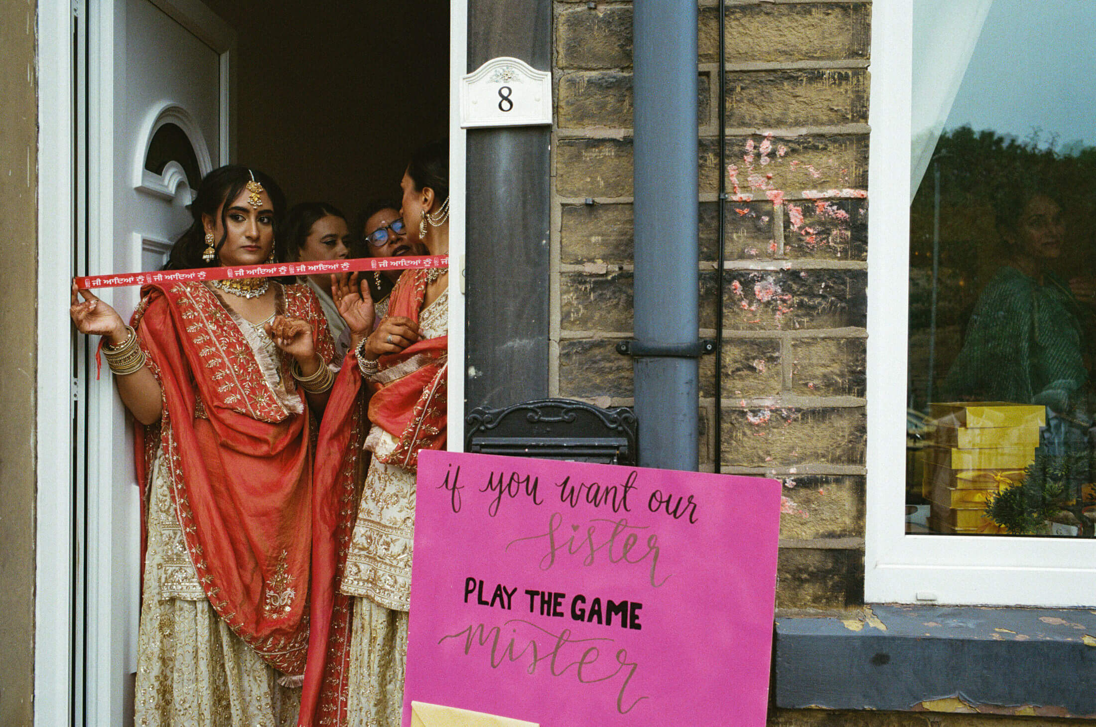 women stand in a red-taped doorway, awaiting the groom for the wedding games to begin