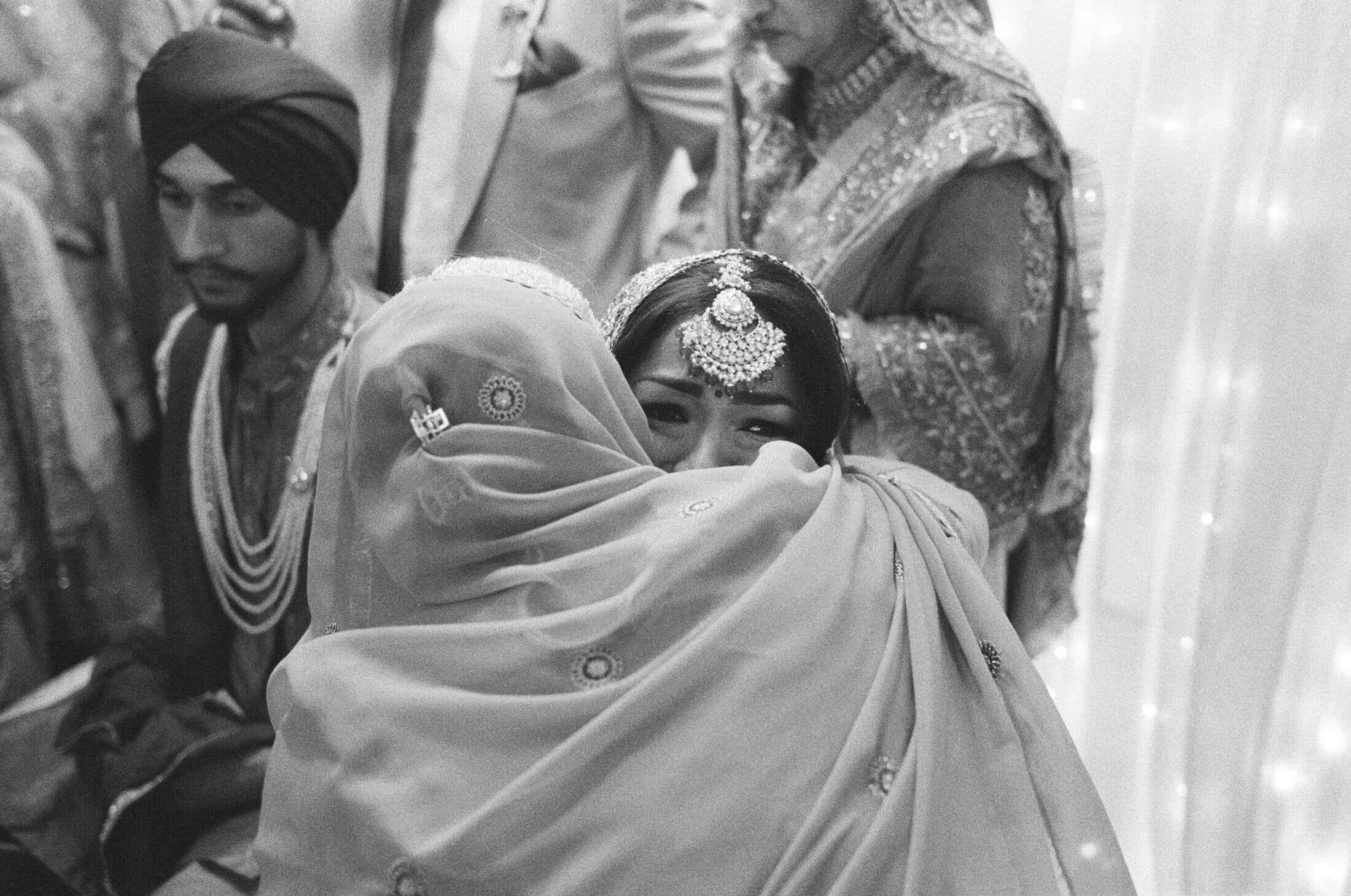 Black and white photograph of a bride embracing a family member, with her eyes visible above their shoulder