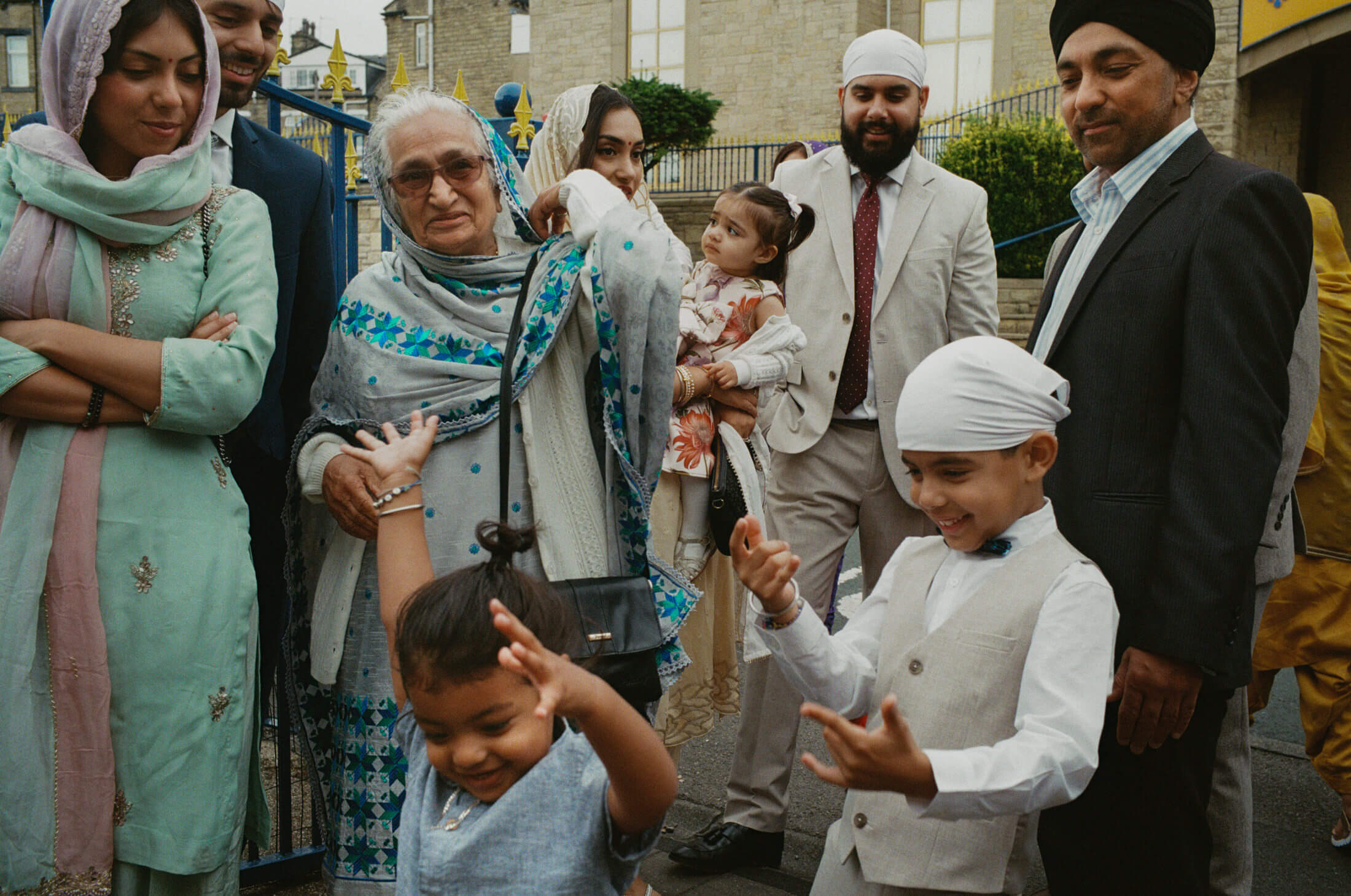Children dancing and playing as family members watch outside a Sikh wedding