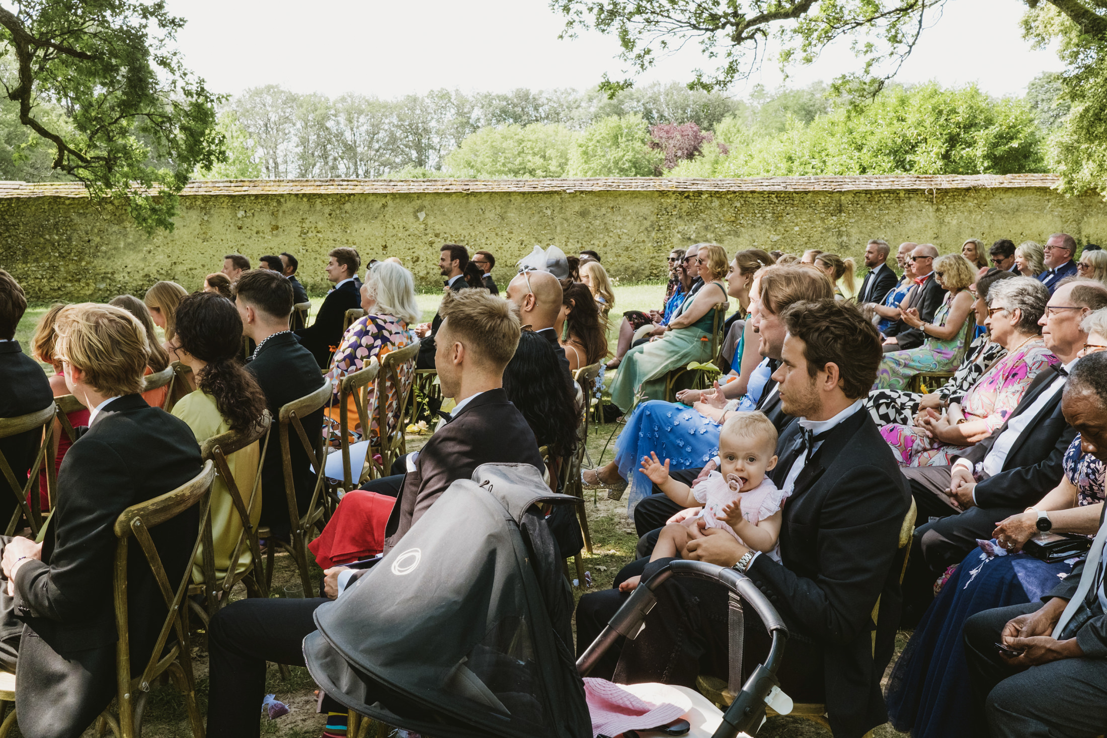 A baby looking at the camera whilst all the other guests watch the ceremony at Chateau du Fey in France