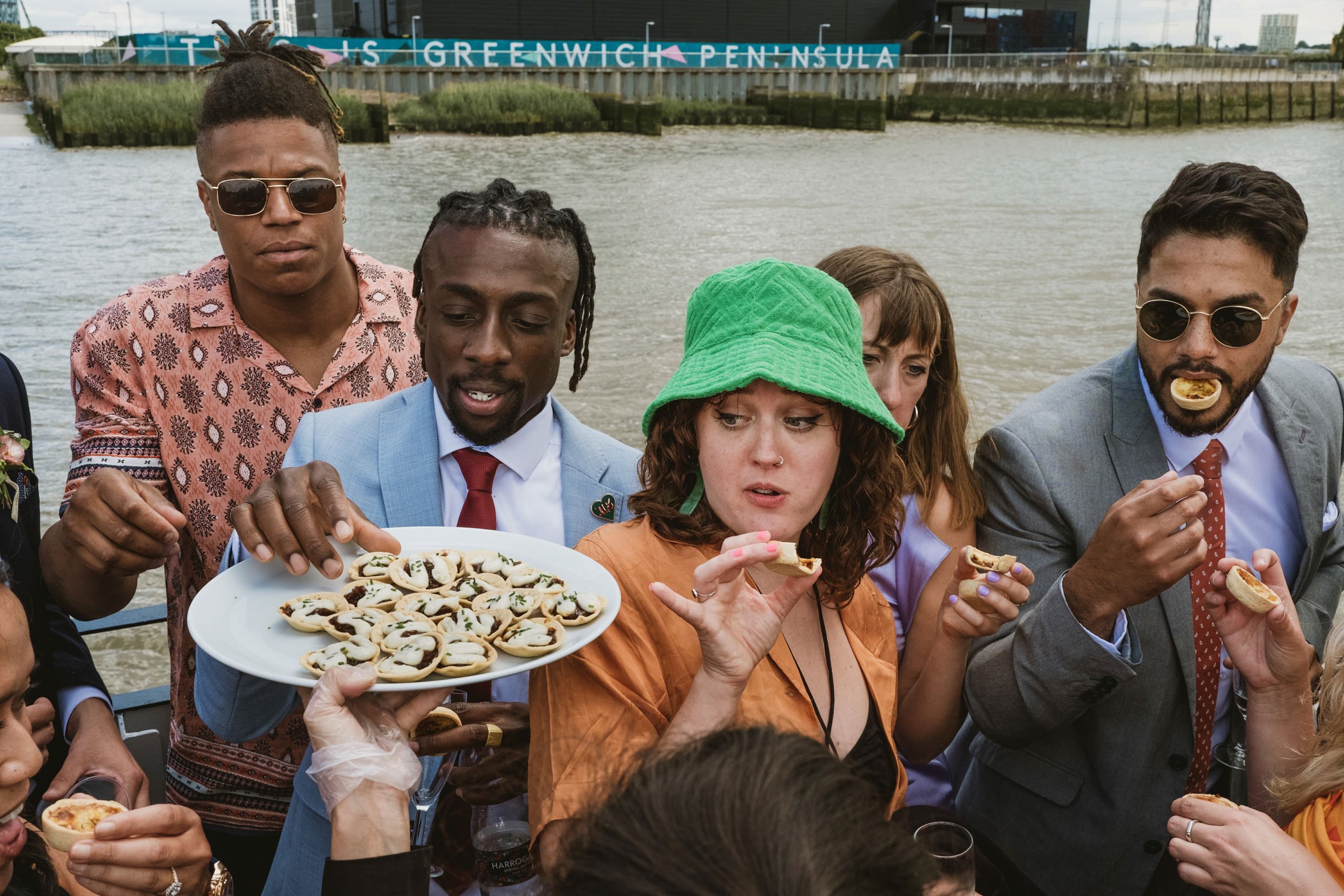Guests share canapés by the Thames at Greenwich Peninsula wedding reception.