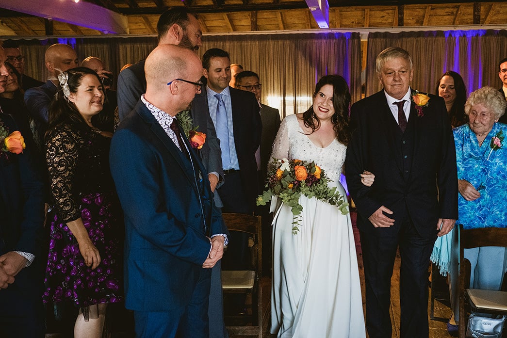 A documentary wedding photograph at East Quay Venue, Whitstable. The frame captures the groom’s reaction as he sees the bride for the first time during the indoor ceremony. The shot focuses on the honest, unscripted emotion and the soft, natural light of the coastal space, documenting the quiet anticipation of the wedding day.