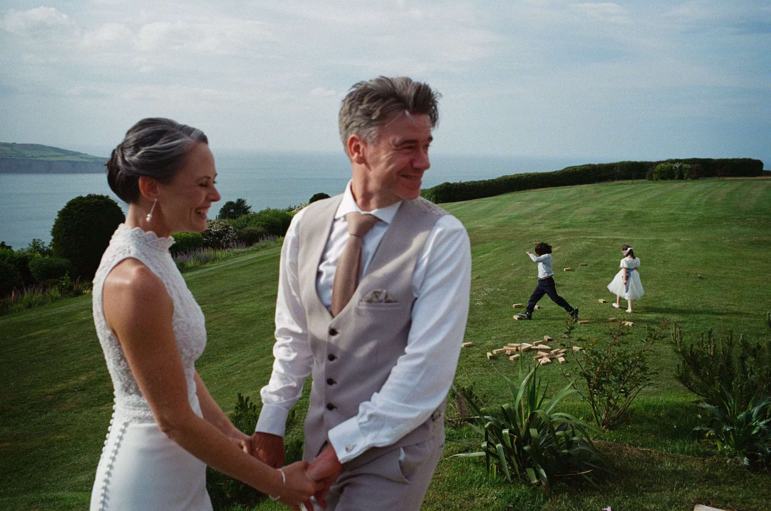 35mm analogue film wedding photograph - bride and groom hold hands in the foreground whilst in the background children play
