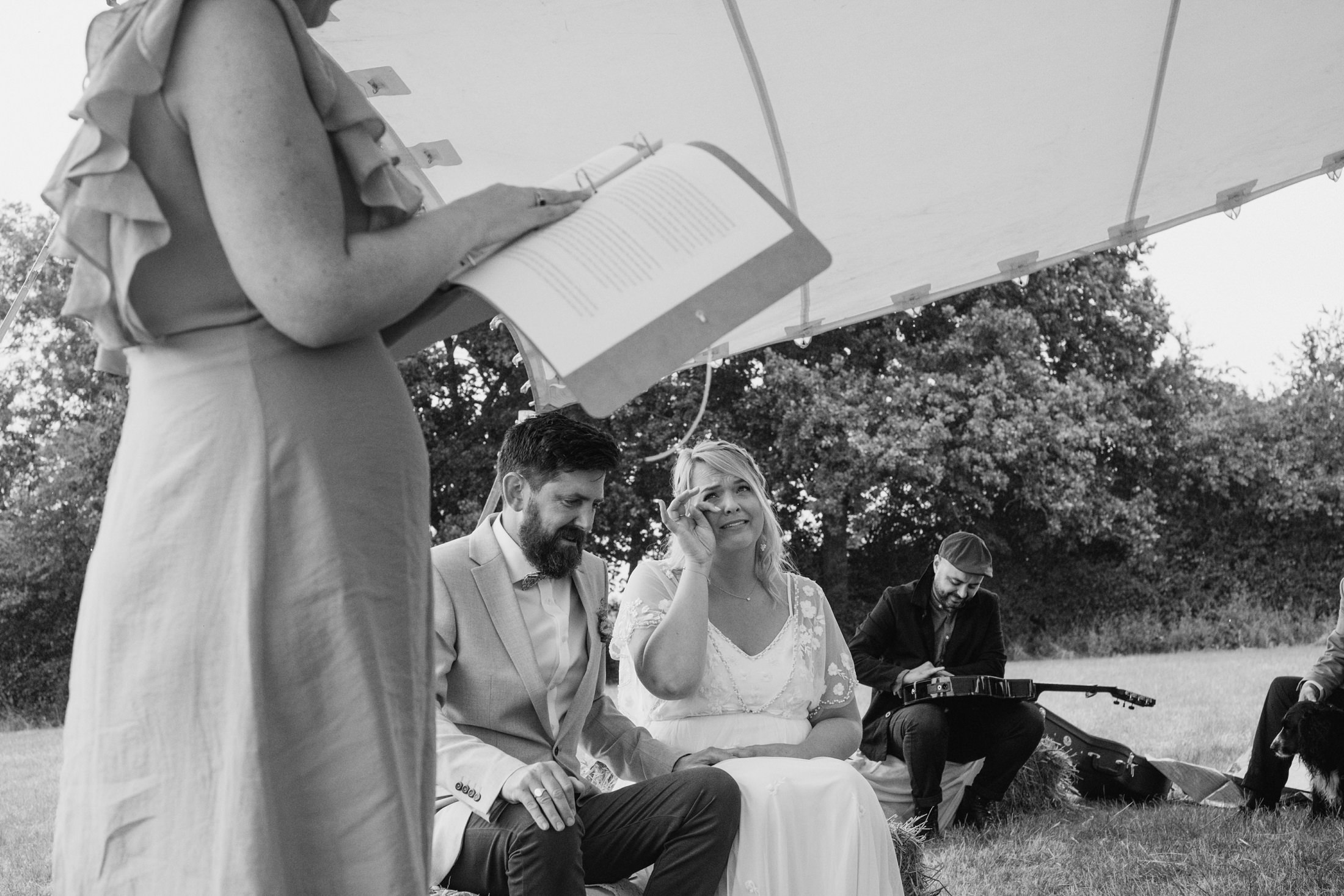 Outdoor wedding ceremony with couple seated, guest reading