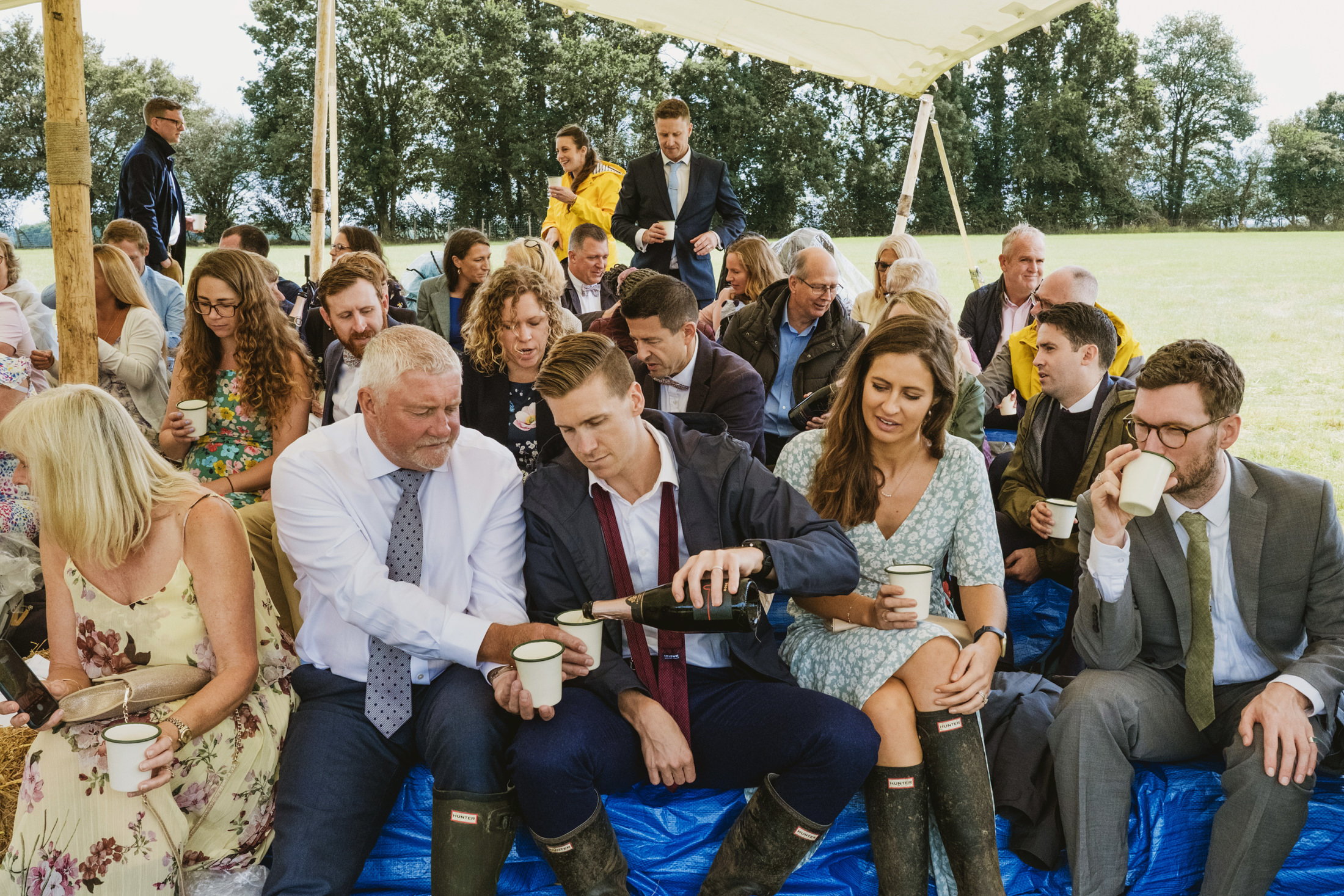 Group enjoying drinks at outdoor event under tent.