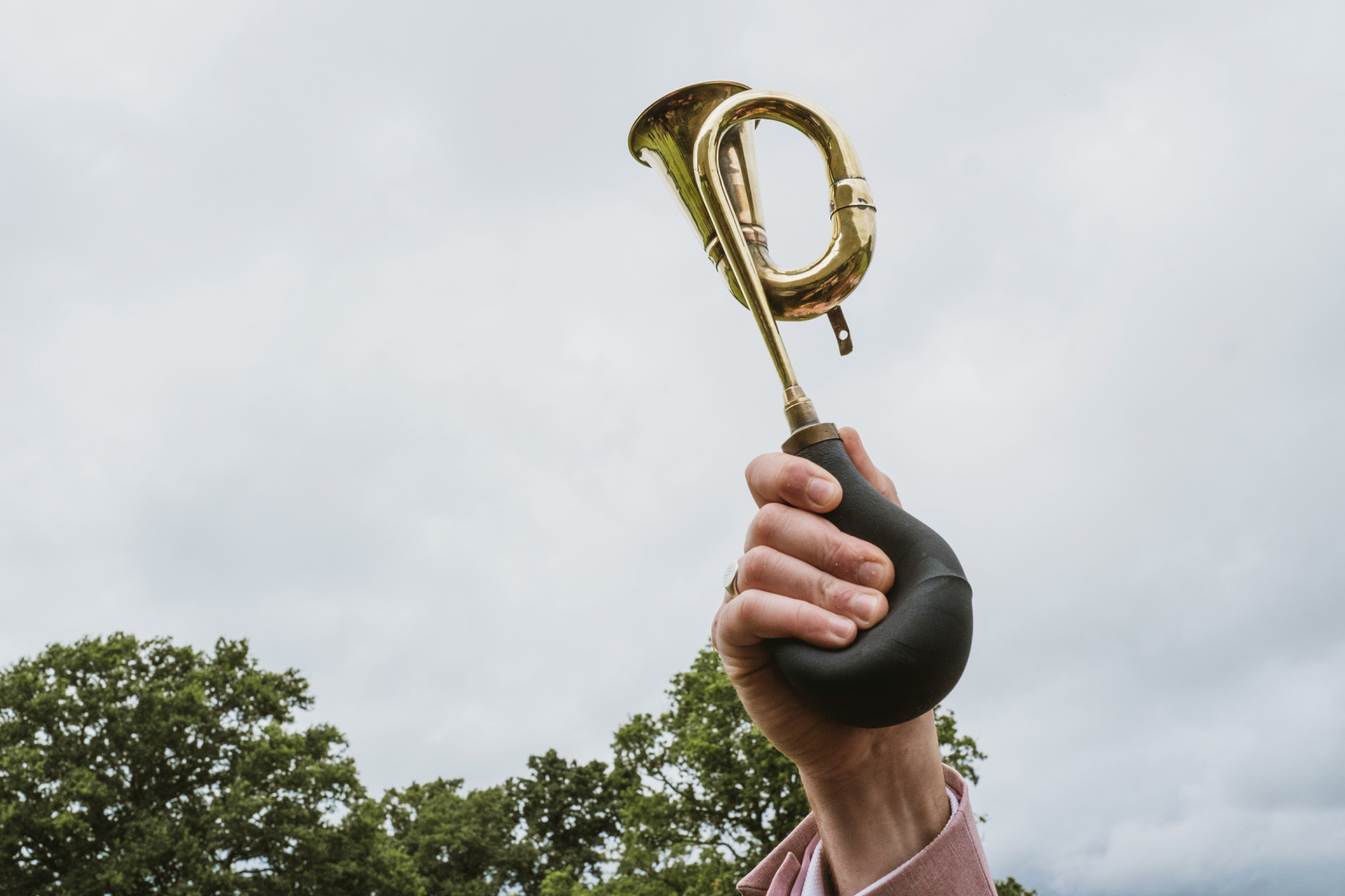Hand holding brass bicycle horn outdoors.