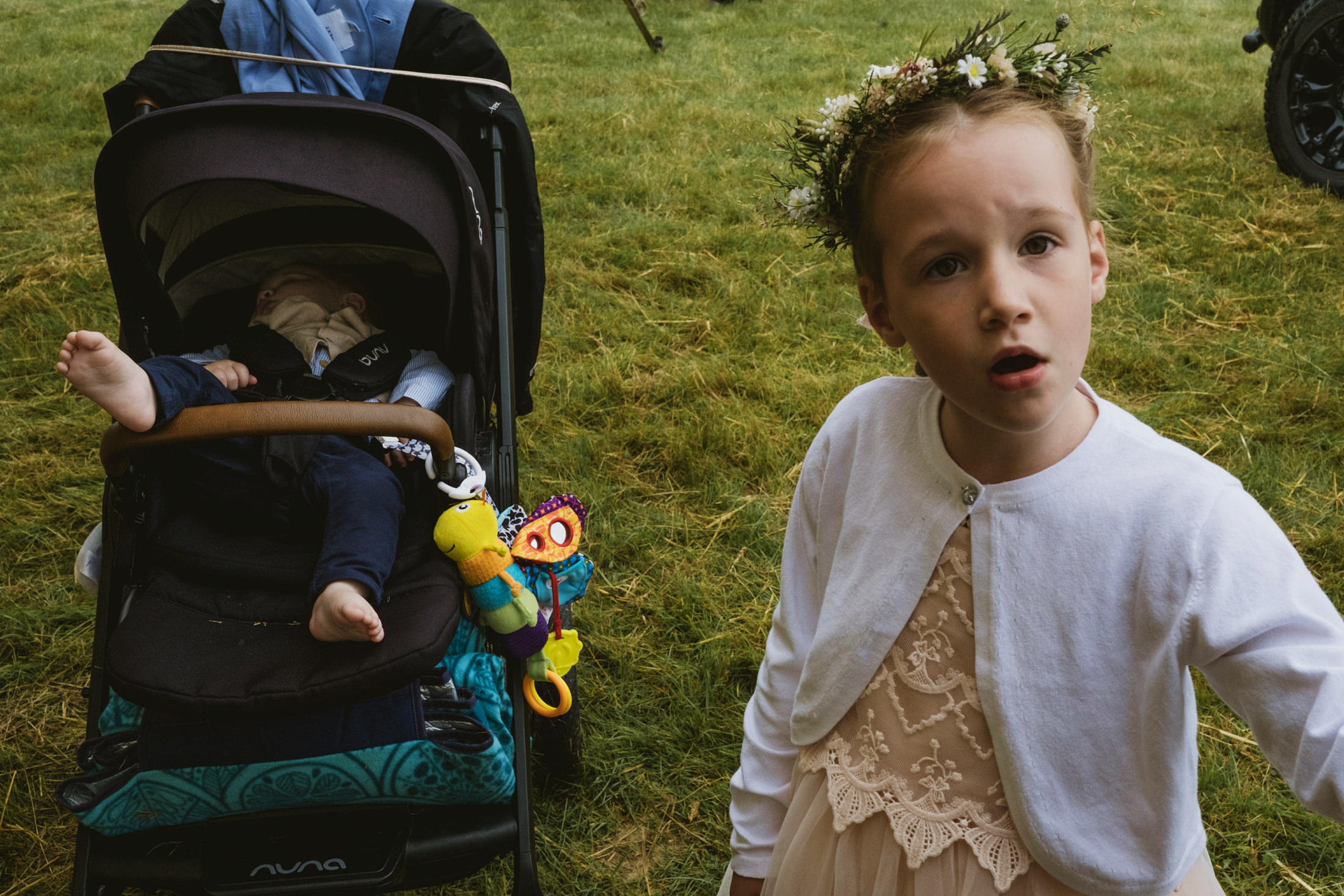 Child with flowers in hair beside sleeping baby.