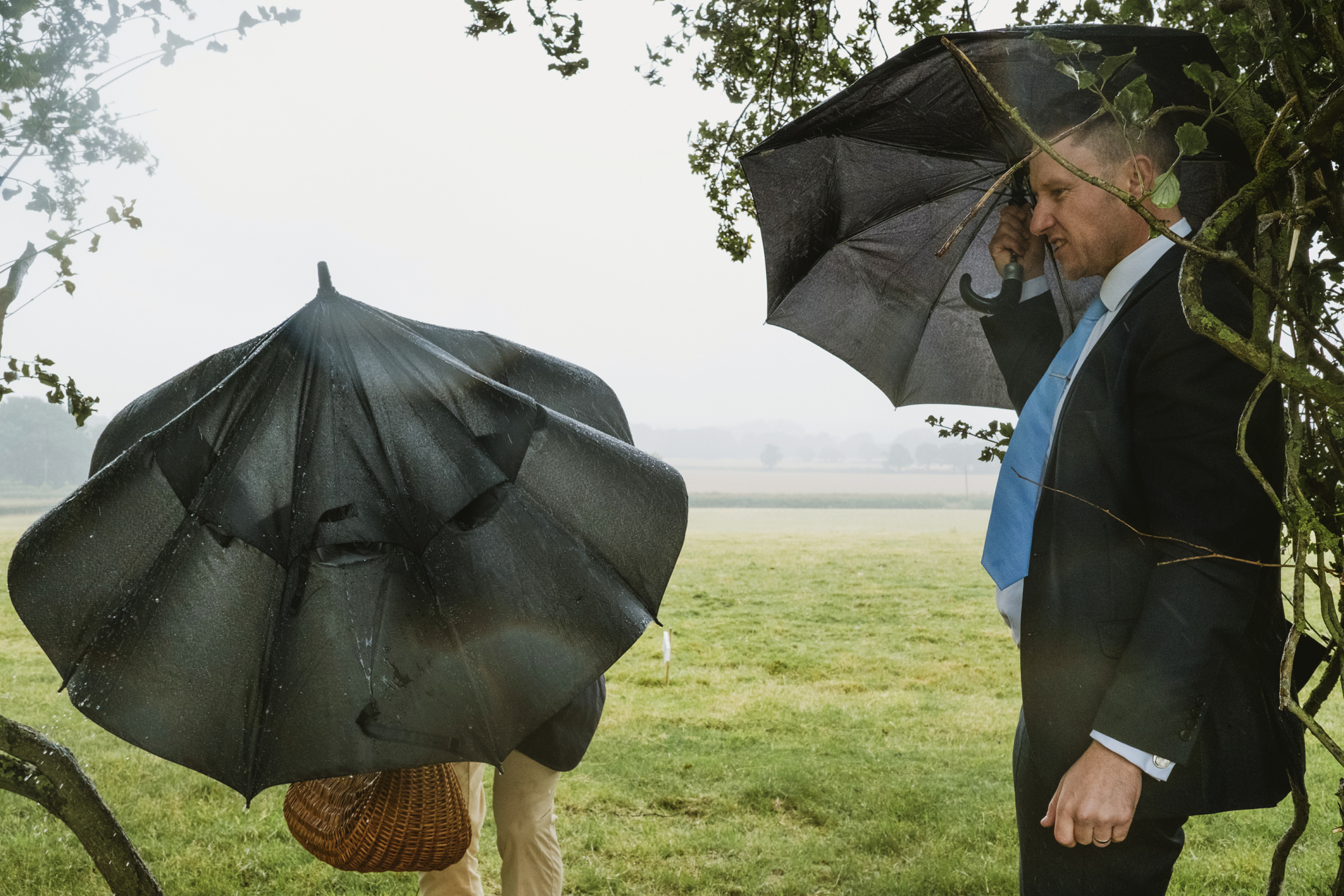 People with umbrellas in a windy, rainy field.