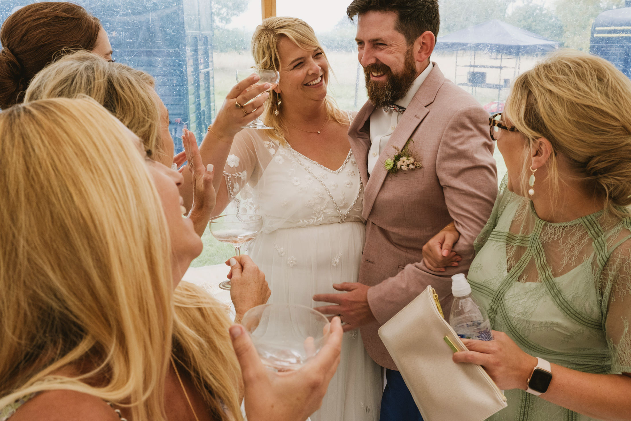 Group celebrating at outdoor wedding, smiling and toasting.