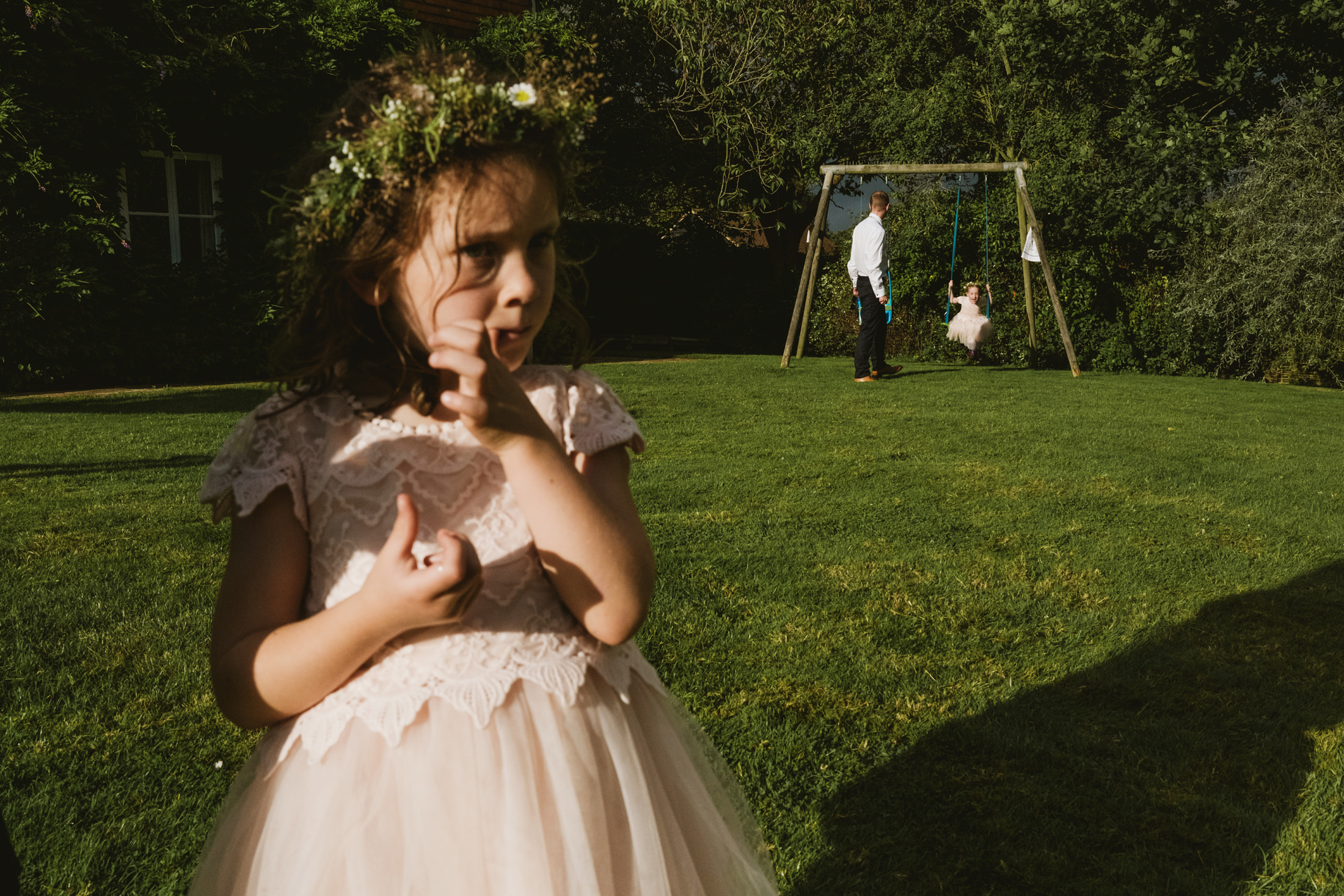 Girl on lawn, child swings in background