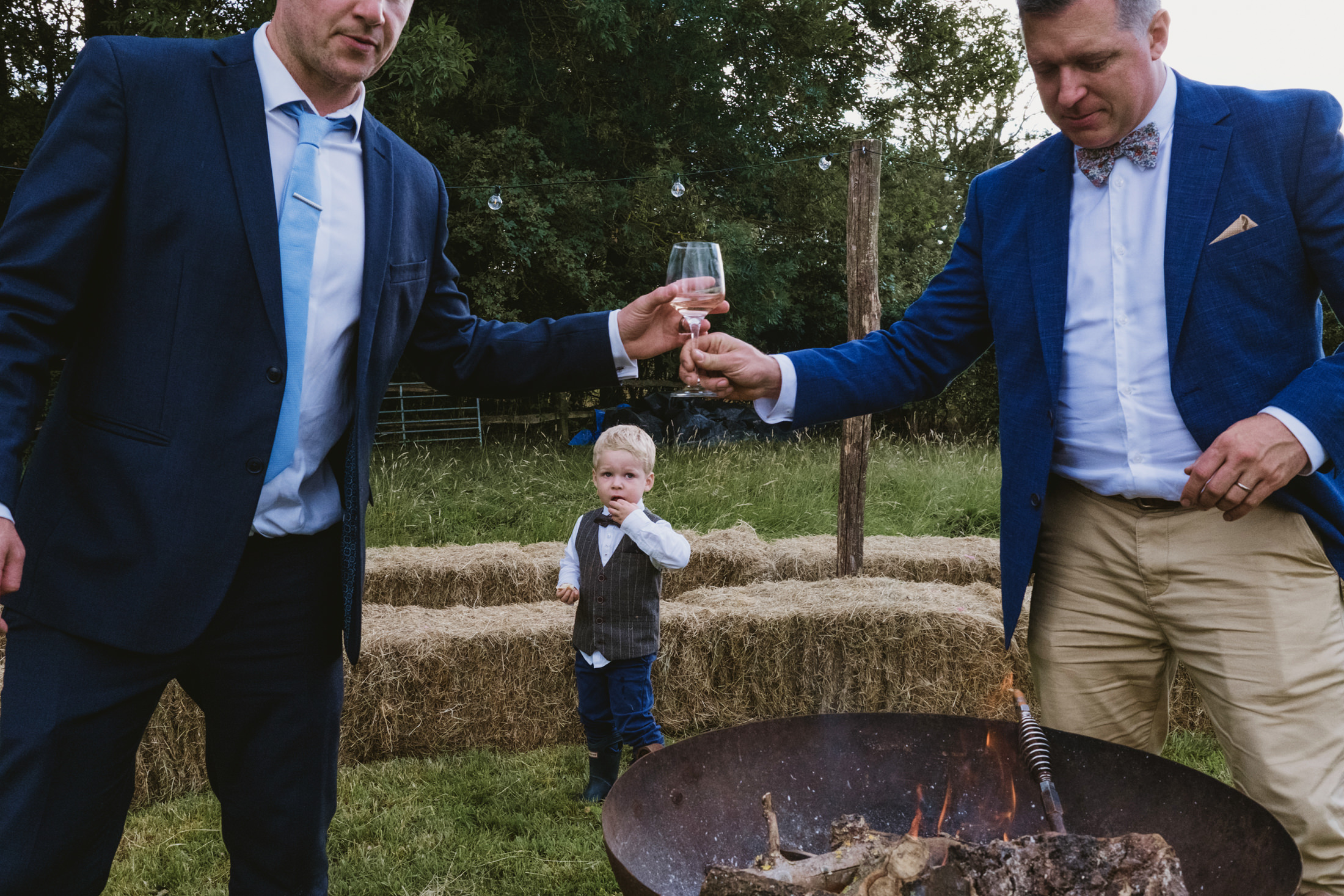 Two men toasting near fire pit outdoors.