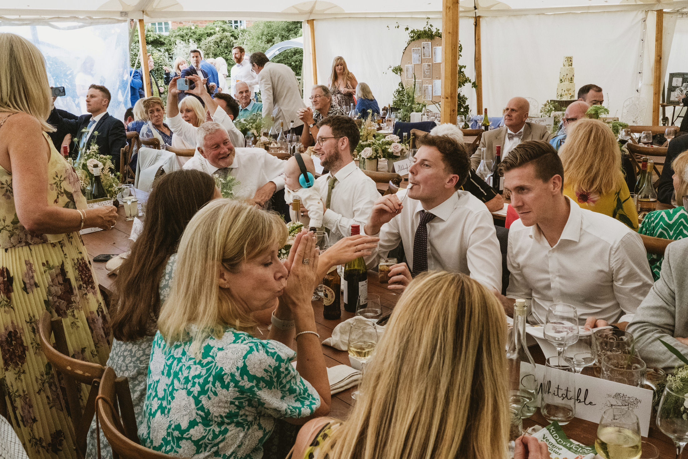 Guests enjoying a lively wedding reception inside marquee.