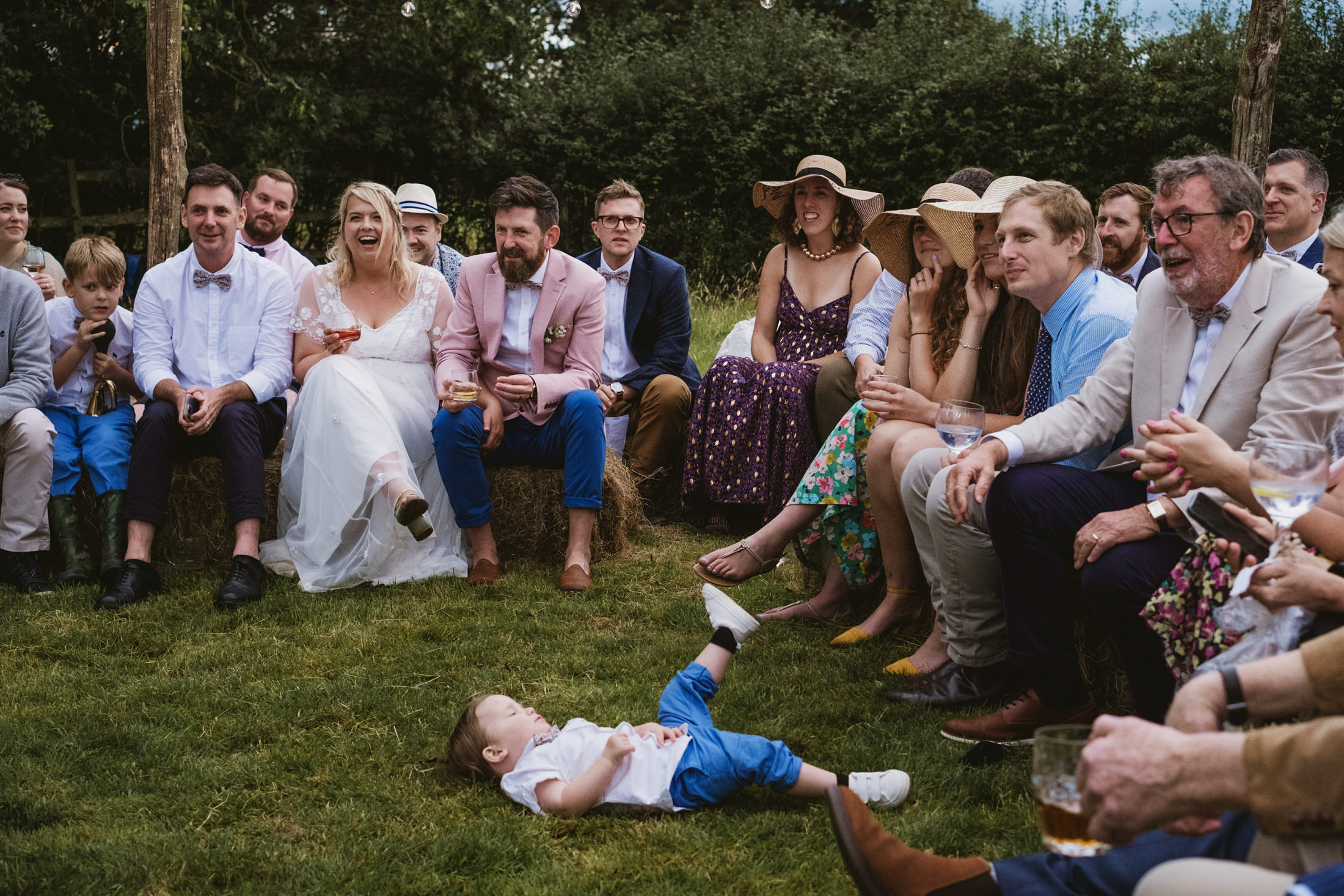 Wedding guests sitting outdoors, child playing on grass.