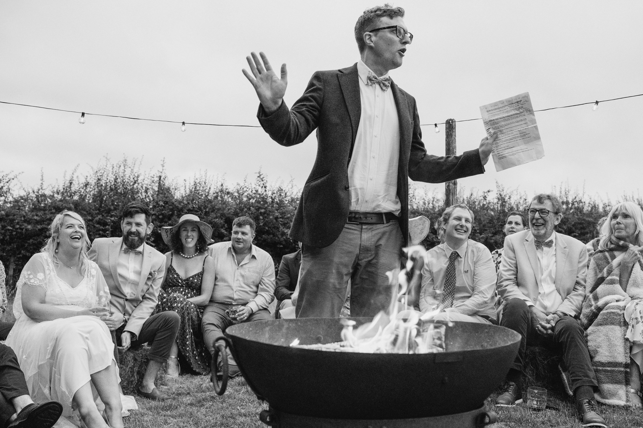 Man giving speech by fire at outdoor gathering.