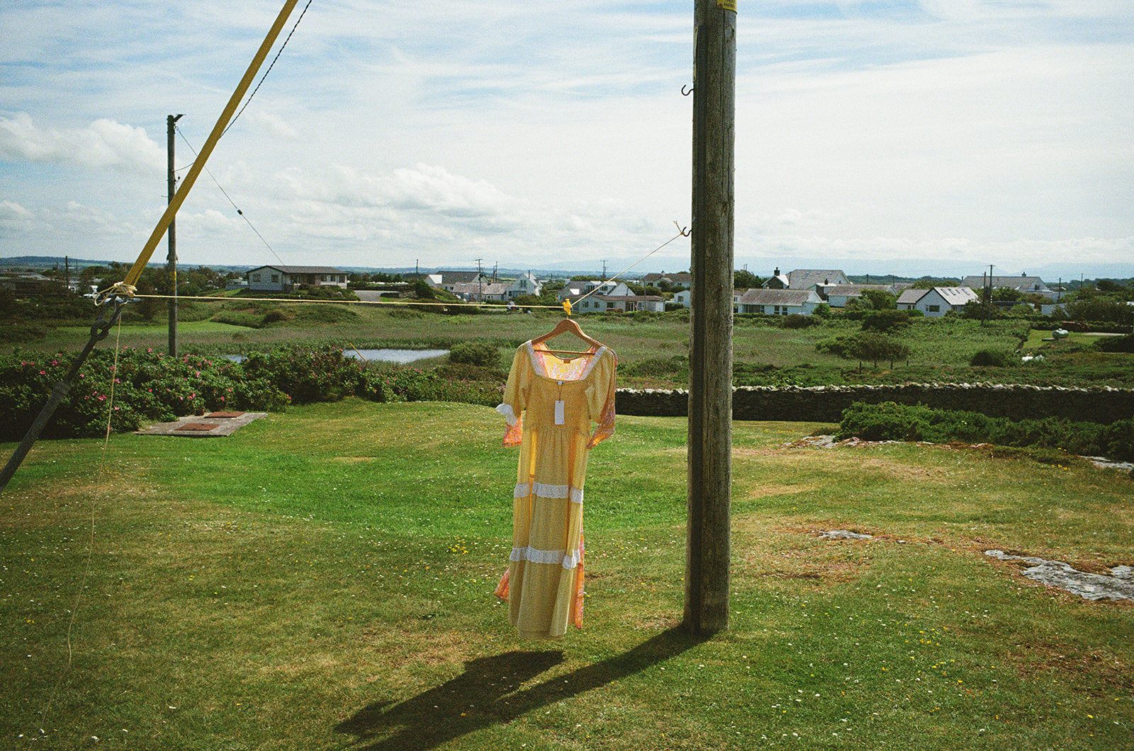 Yellow wedding dress hanging on a garden line, sunlight over quiet coastal village.