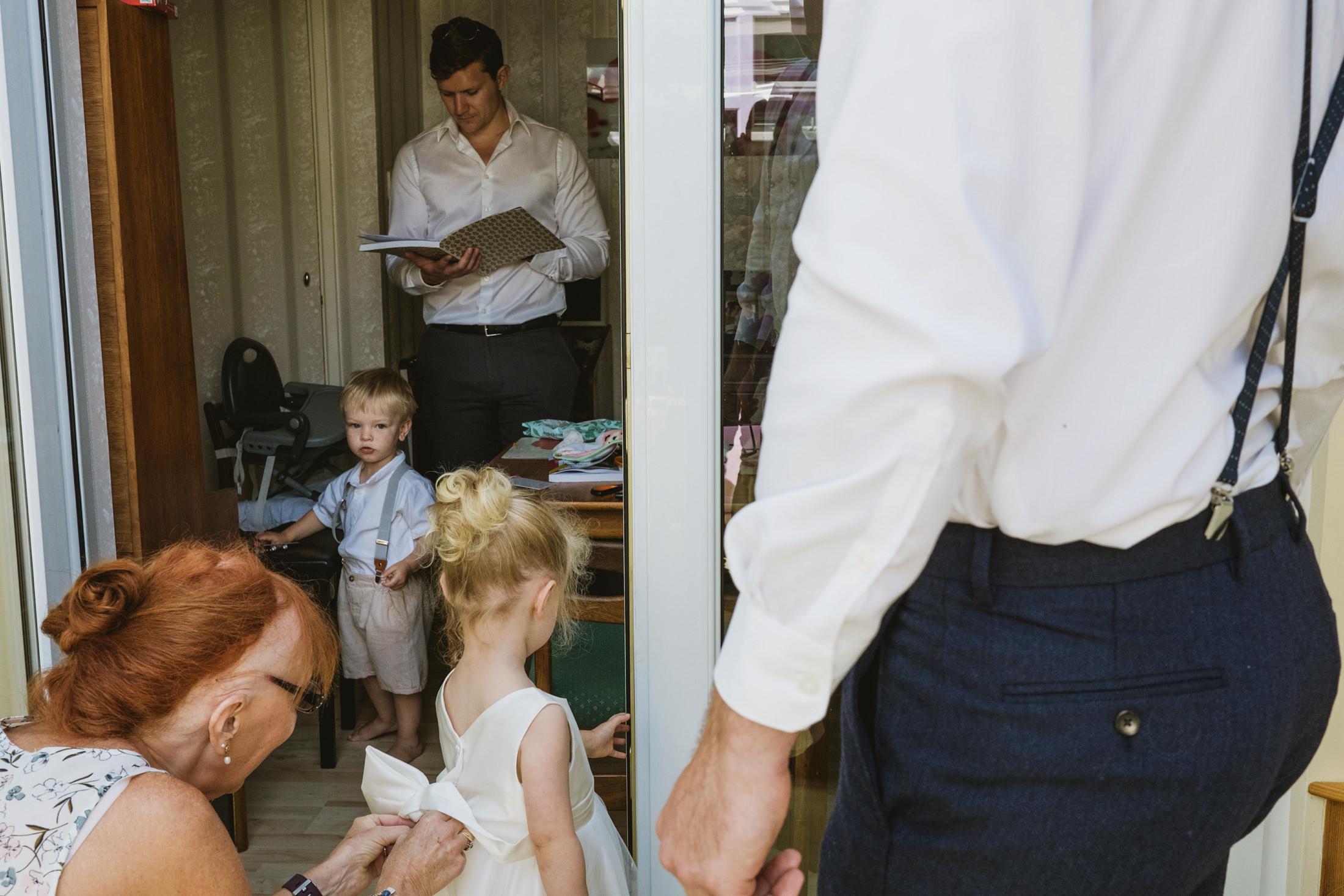 Man reads, woman adjusts child's dress indoors.