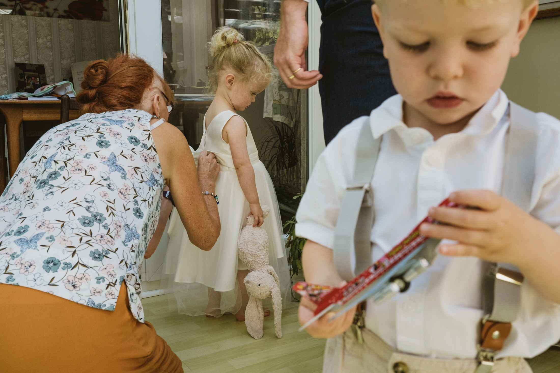 Woman adjusting girl's dress, boy holding toy.