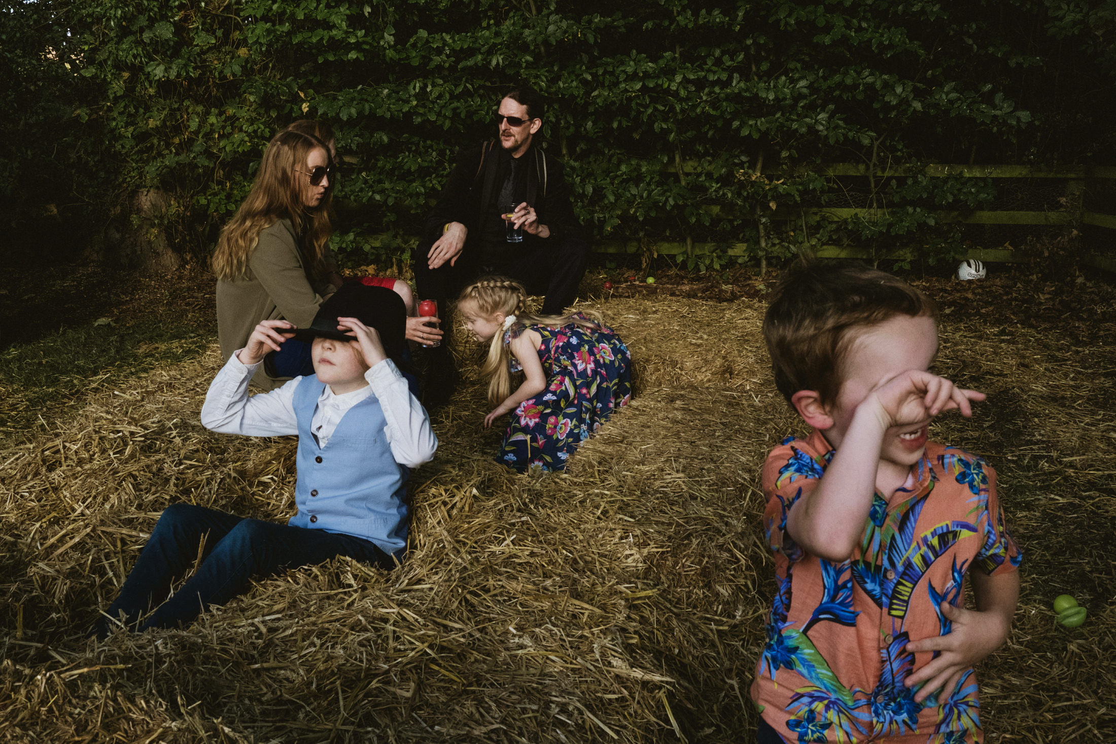 Children and adults playing on hay bales outdoors.