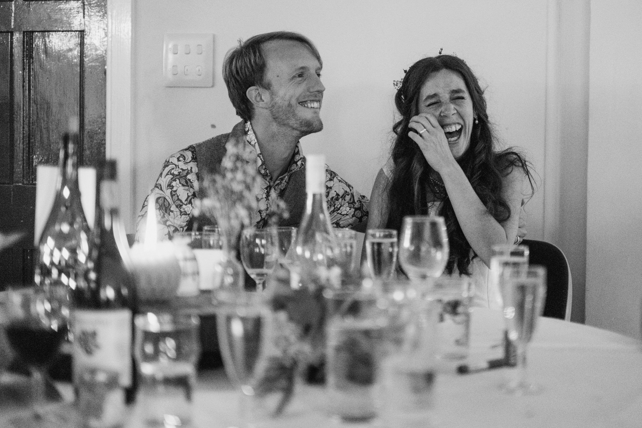 Smiling couple at a celebration, glasses on table.