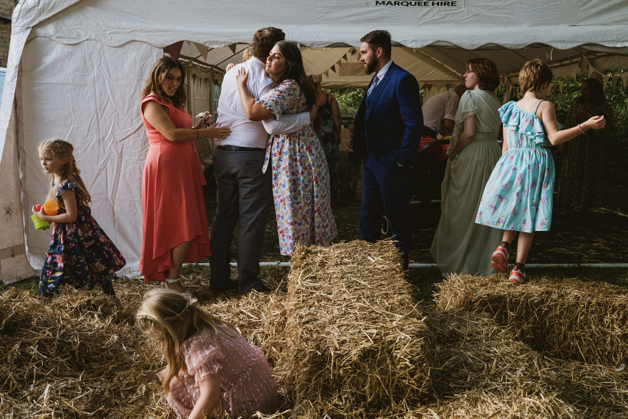 People at outdoor event with hay bales and marquee.