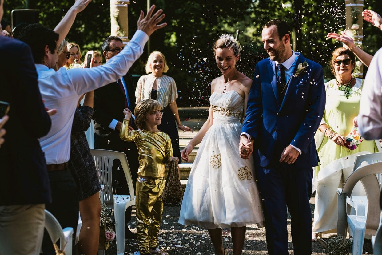 Pump House Battersea Park London Bride and groom leaving the ceremony gold ninja boy throwing confetti
