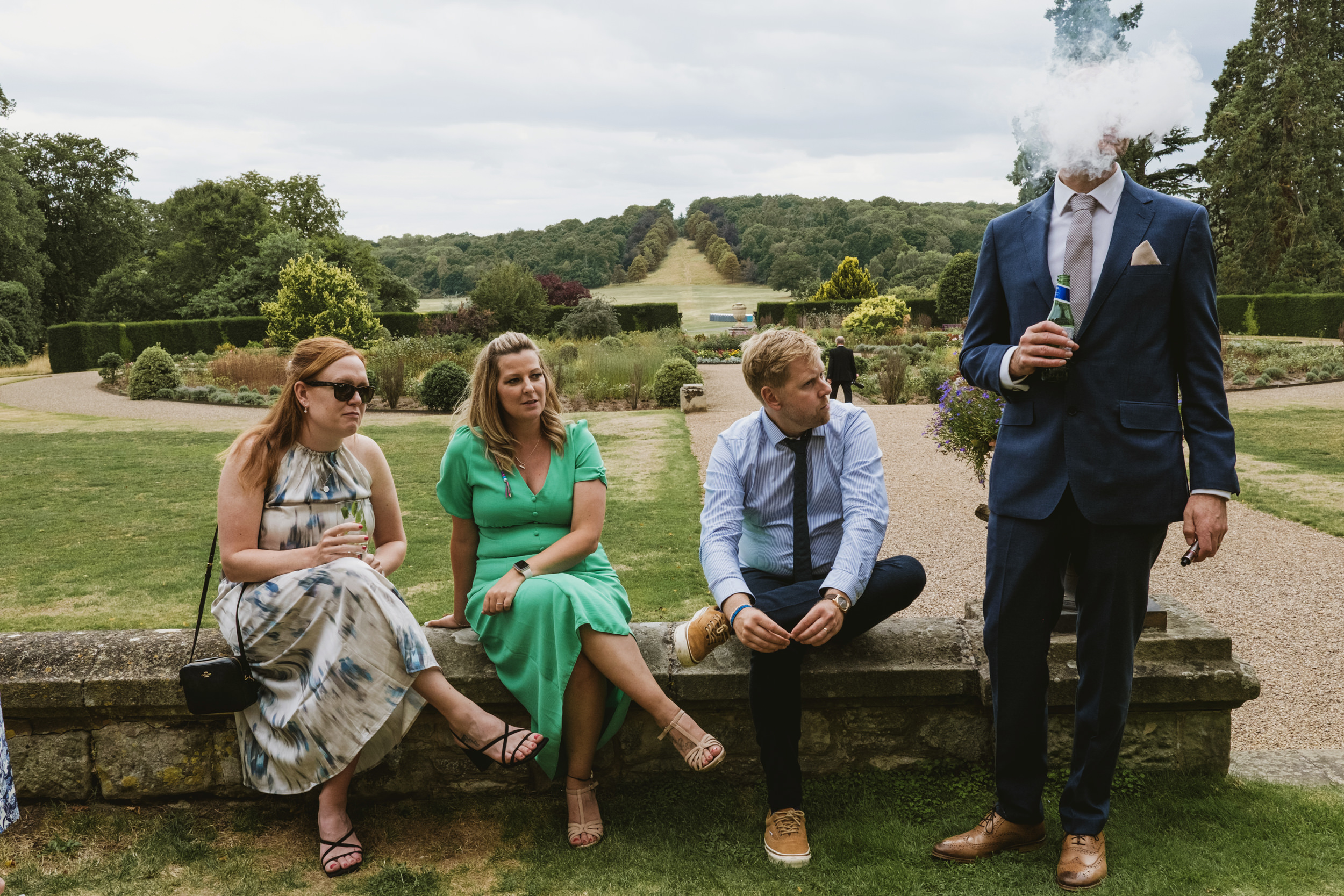 Group sitting in garden, man vaping with suit.
