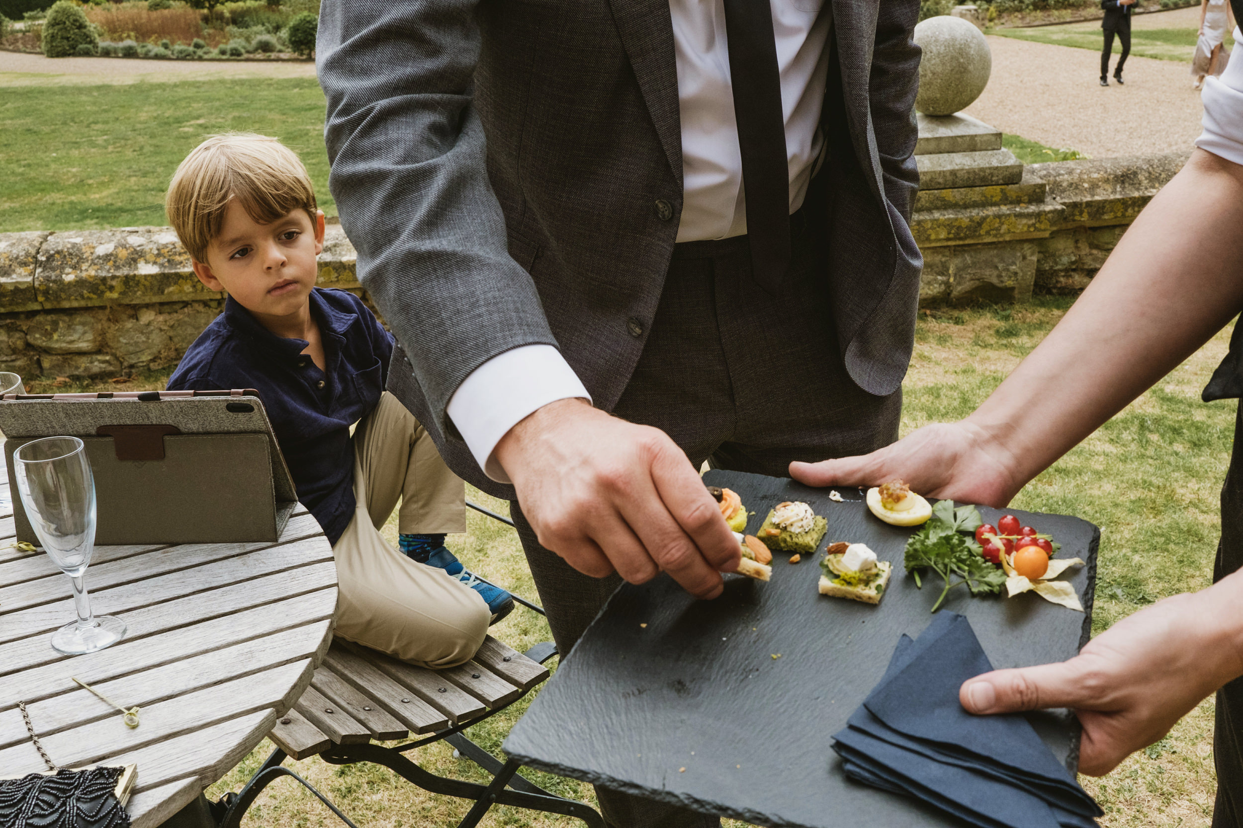 Child at table with adults serving appetisers outdoors.