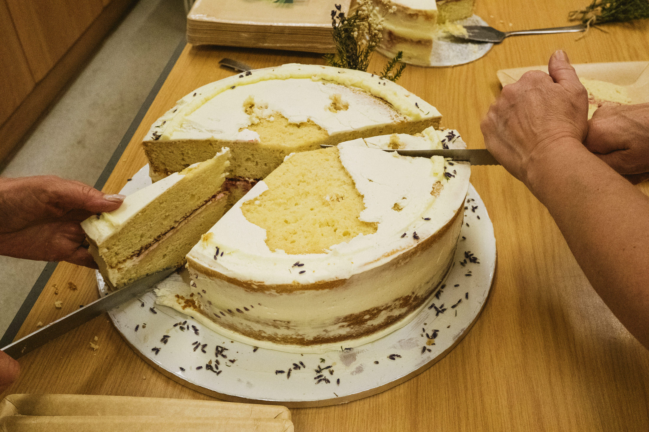 Slicing a layered vanilla cake with lavender topping.