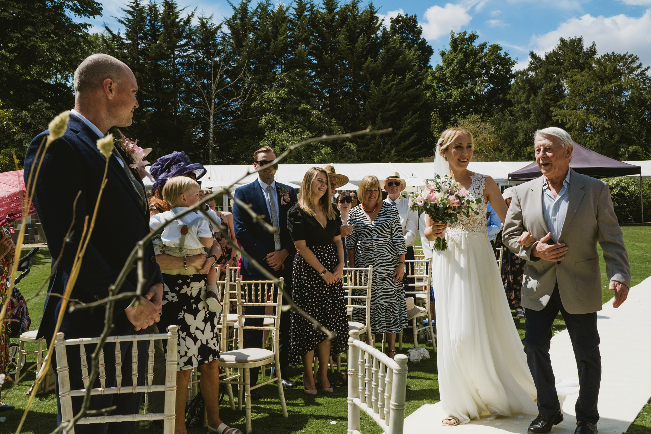 Bride walks down outdoor wedding aisle with father.