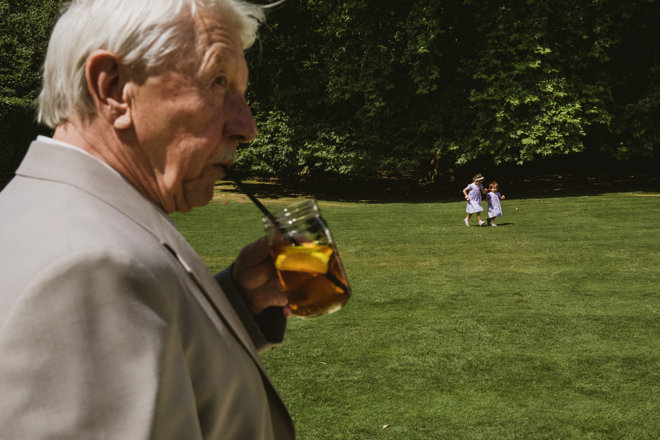 Man drinking iced tea at park, children in background.