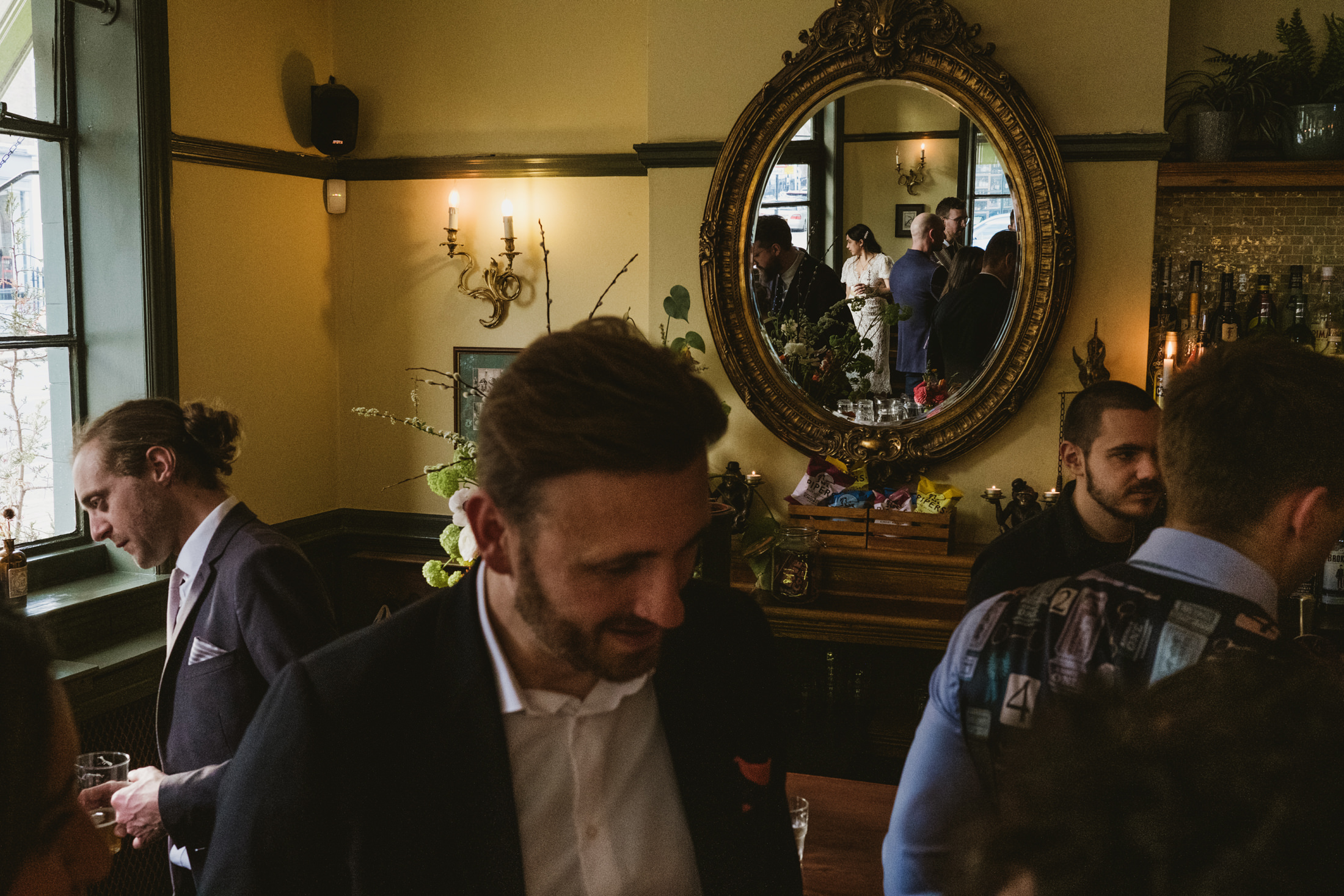 People mingling at elegant bar with large mirror.
