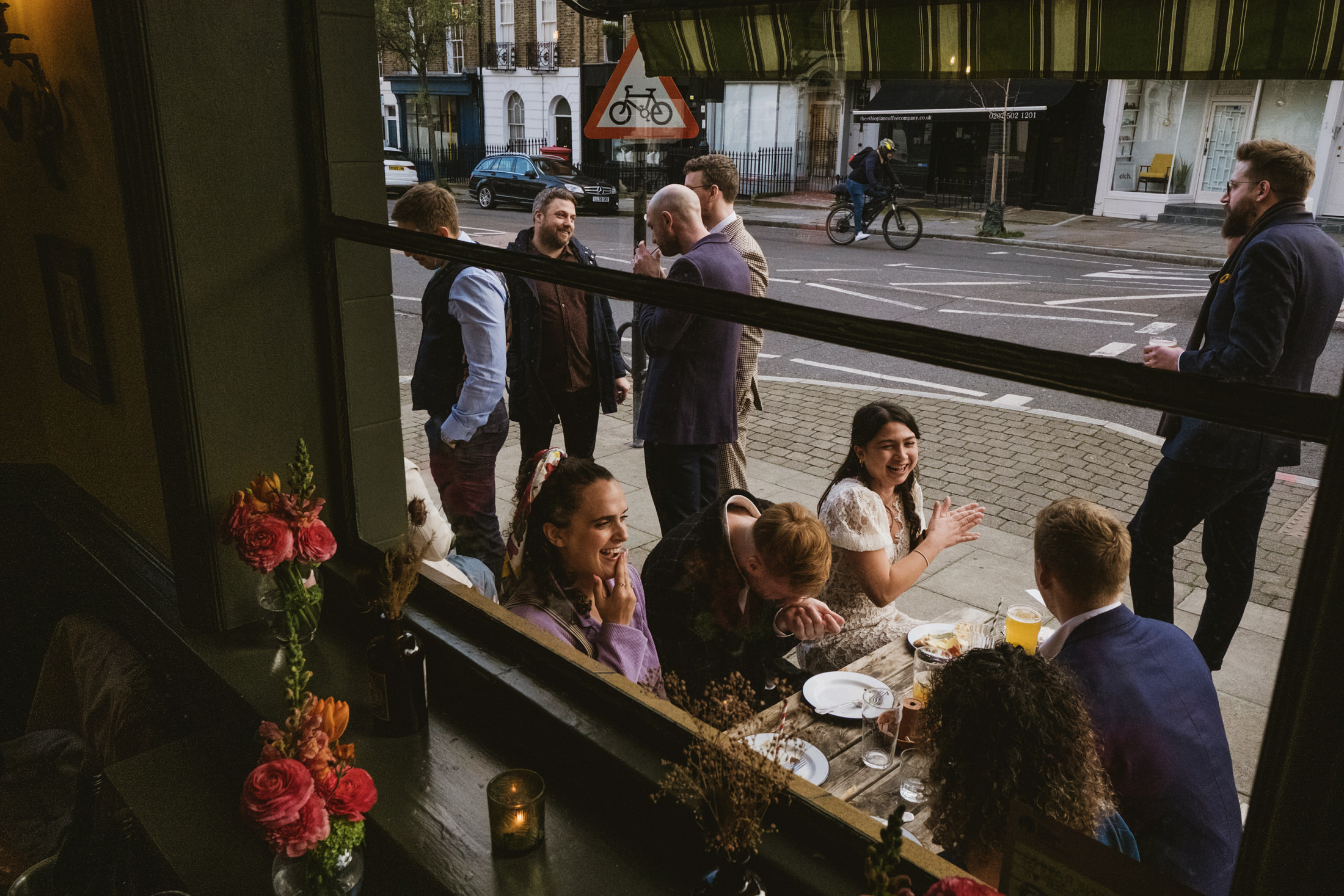 People socialising outside a café, cheerful atmosphere. Beyond the perfect: haphazard bouquets and real wedding atmosphere in a London pub.