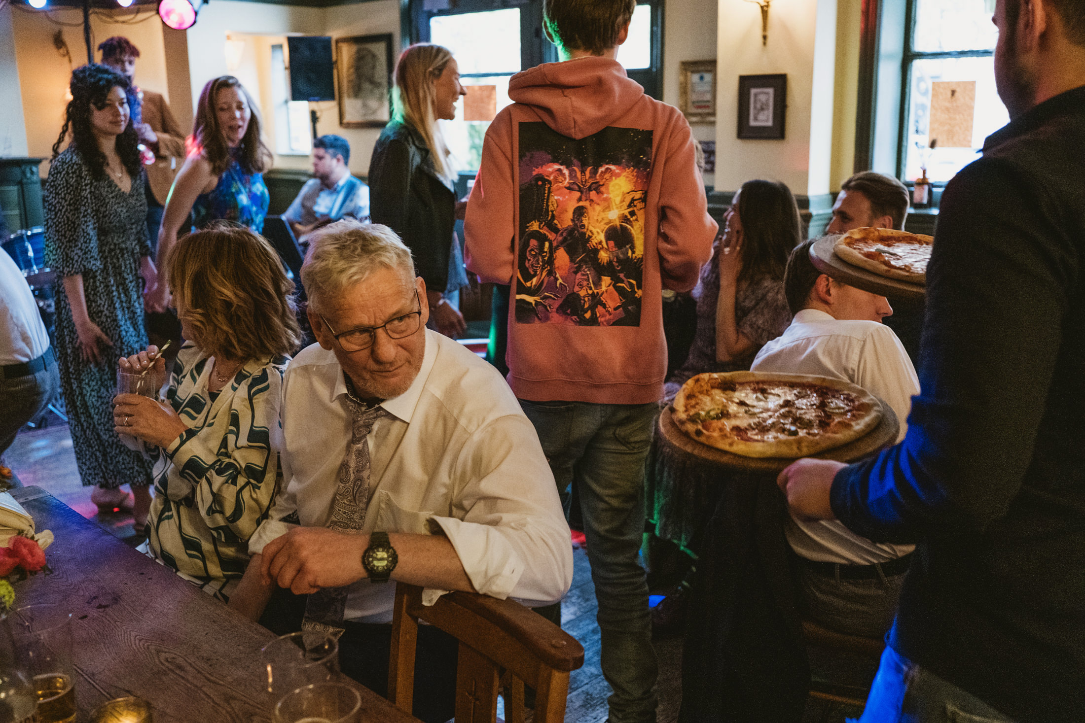 Crowded pub scene with people and pizzas.