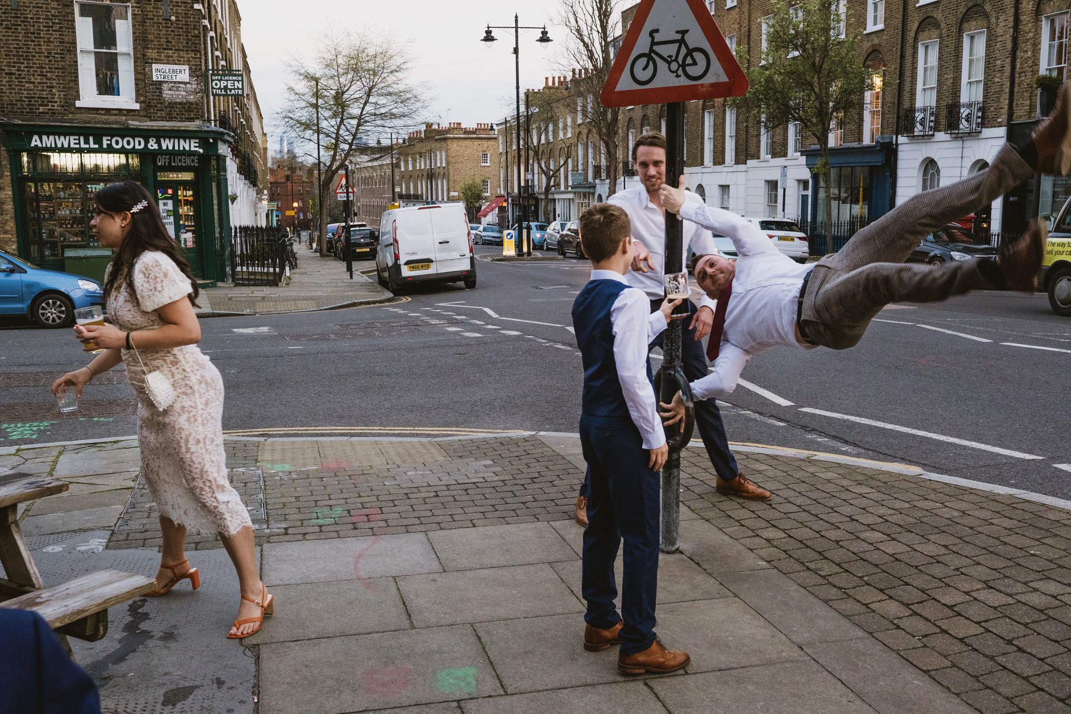 People playing around a street sign in cityscape. Authentic, unposed wedding photography at The George & Monkey; focusing on the joy of the present moment.