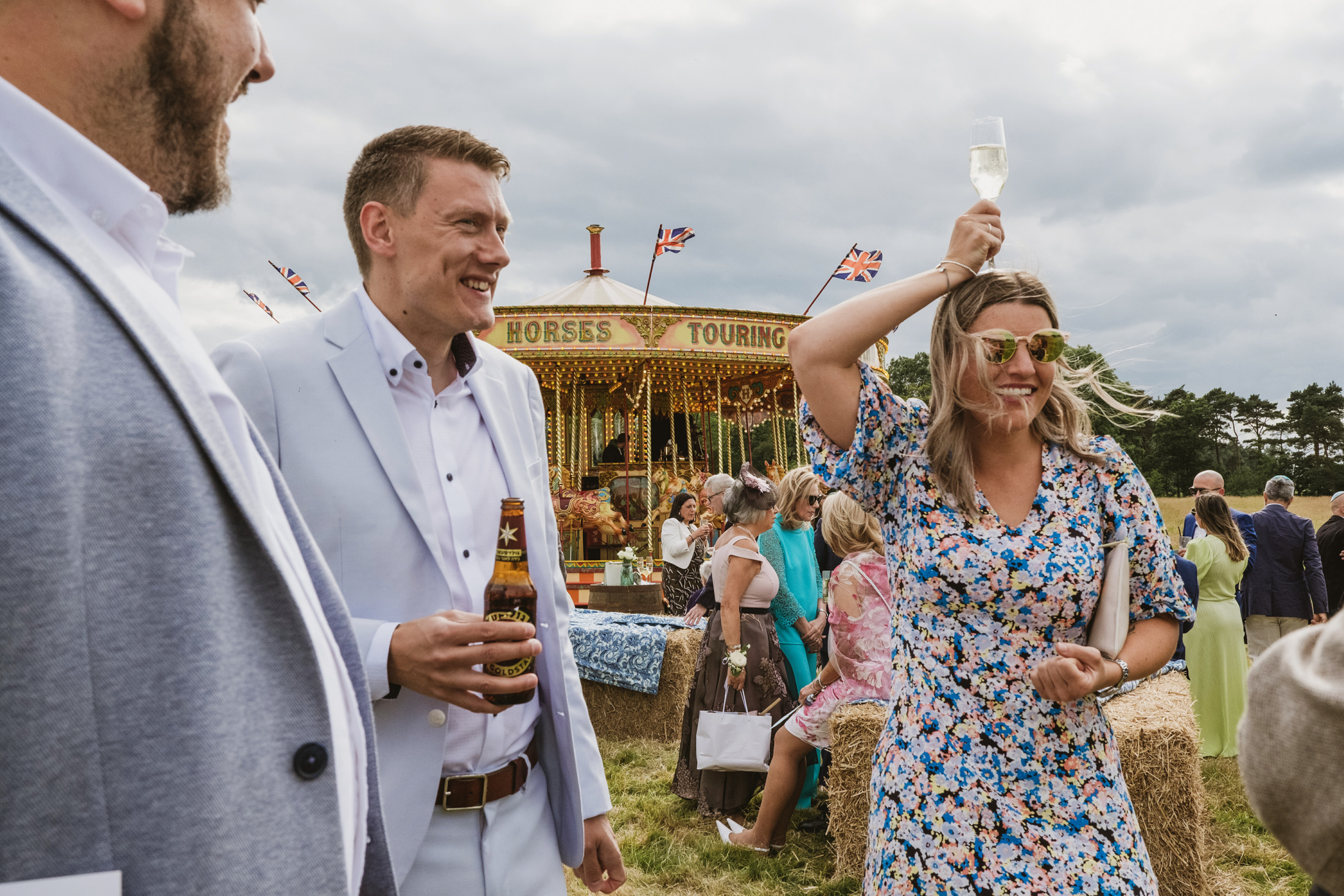 Outdoor festival with carousel, people socialising, enjoying drinks.