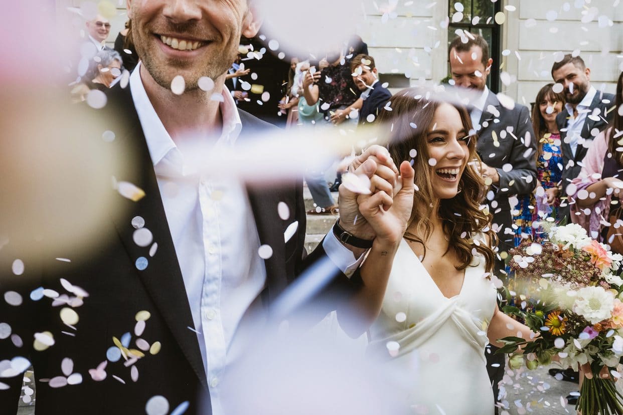A high-energy confetti explosion as the bride and groom walk down the iconic exterior stone steps of the Town Hall Hotel in Bethnal Green. A documentary wedding photograph capturing the raw joy and East London atmosphere of the celebration.