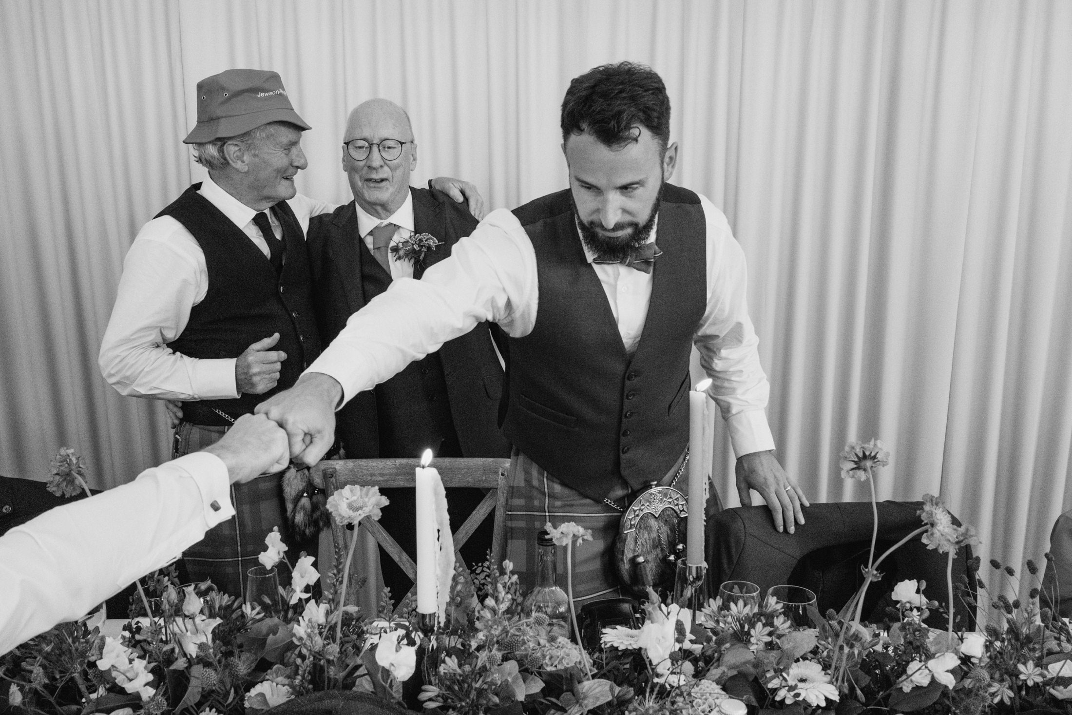 Men in kilts at formal event, fist bumping.