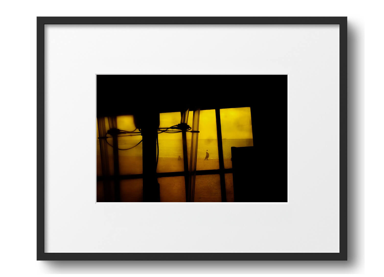 A lone figure walks across a golden beach, seen through dark window frames and trailing cables.