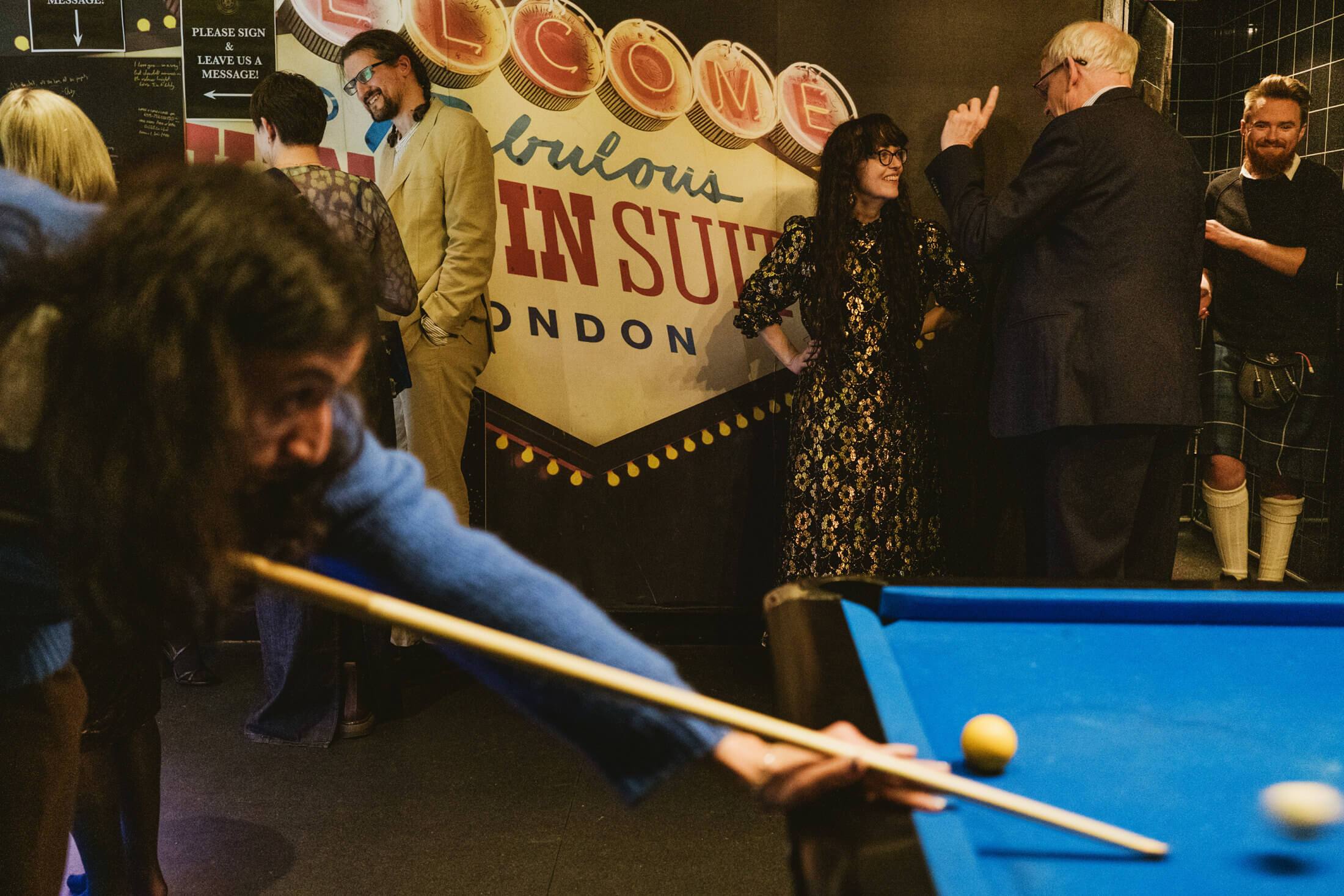 Guests chat and laugh beside a pool table during a lively wedding reception.