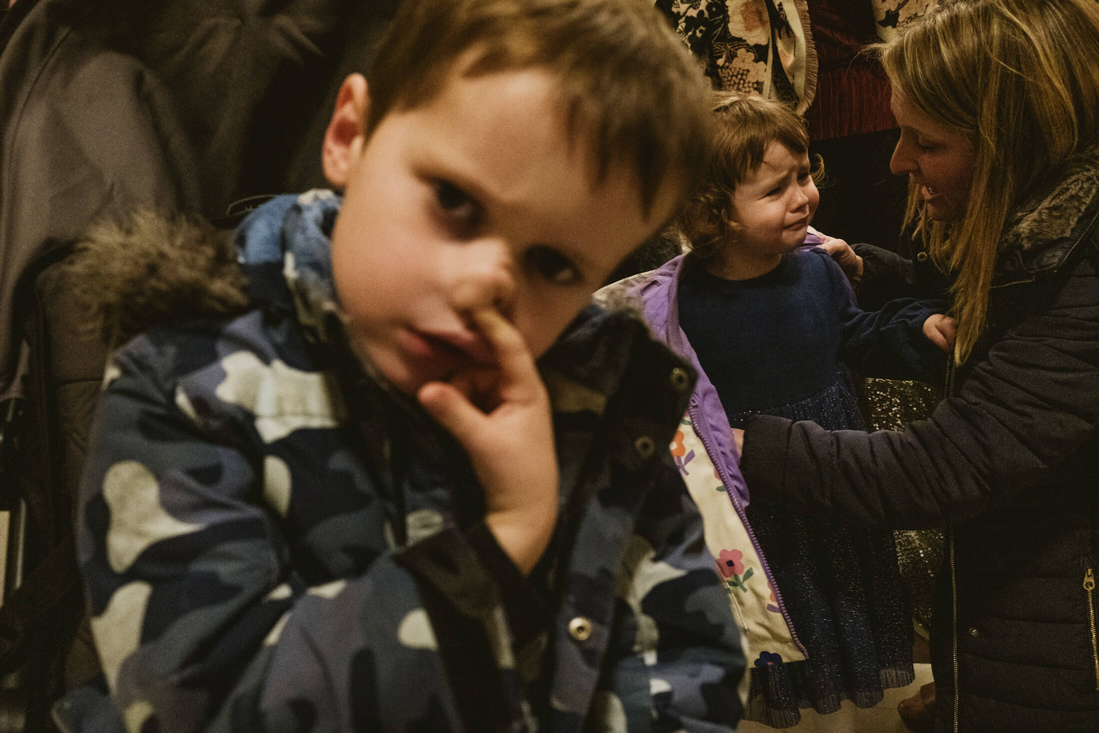 Child touches his nose as a woman comforts a tearful girl during a quiet wedding moment