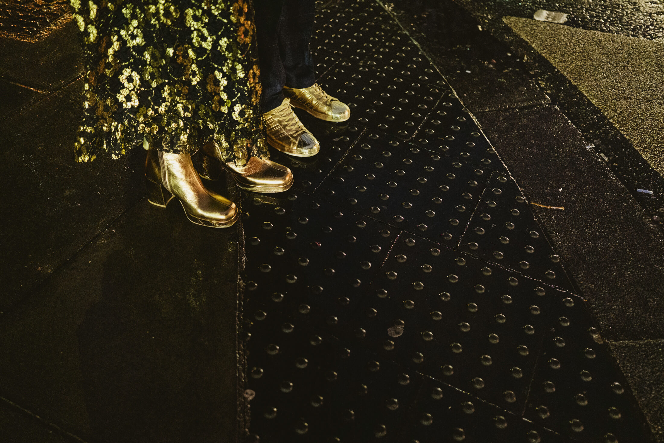 Gold boots and trainers on rain-darkened metal steps during documentary wedding photography.