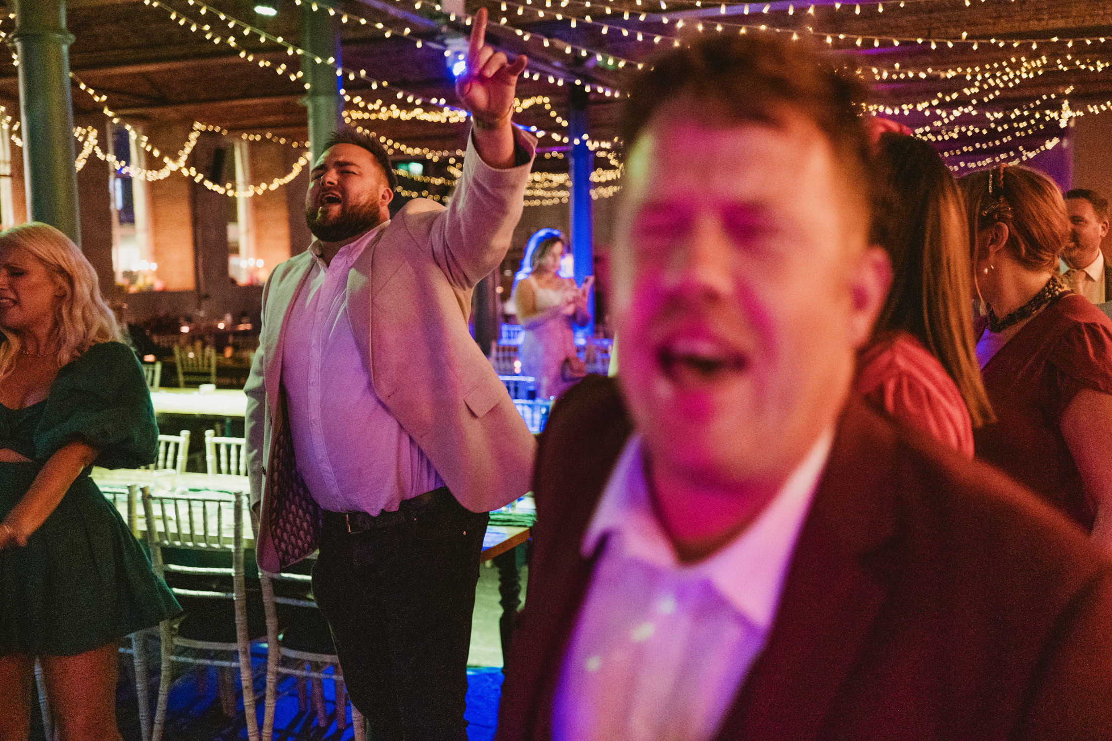 Guests singing and dancing beneath fairy lights at a lively wedding reception