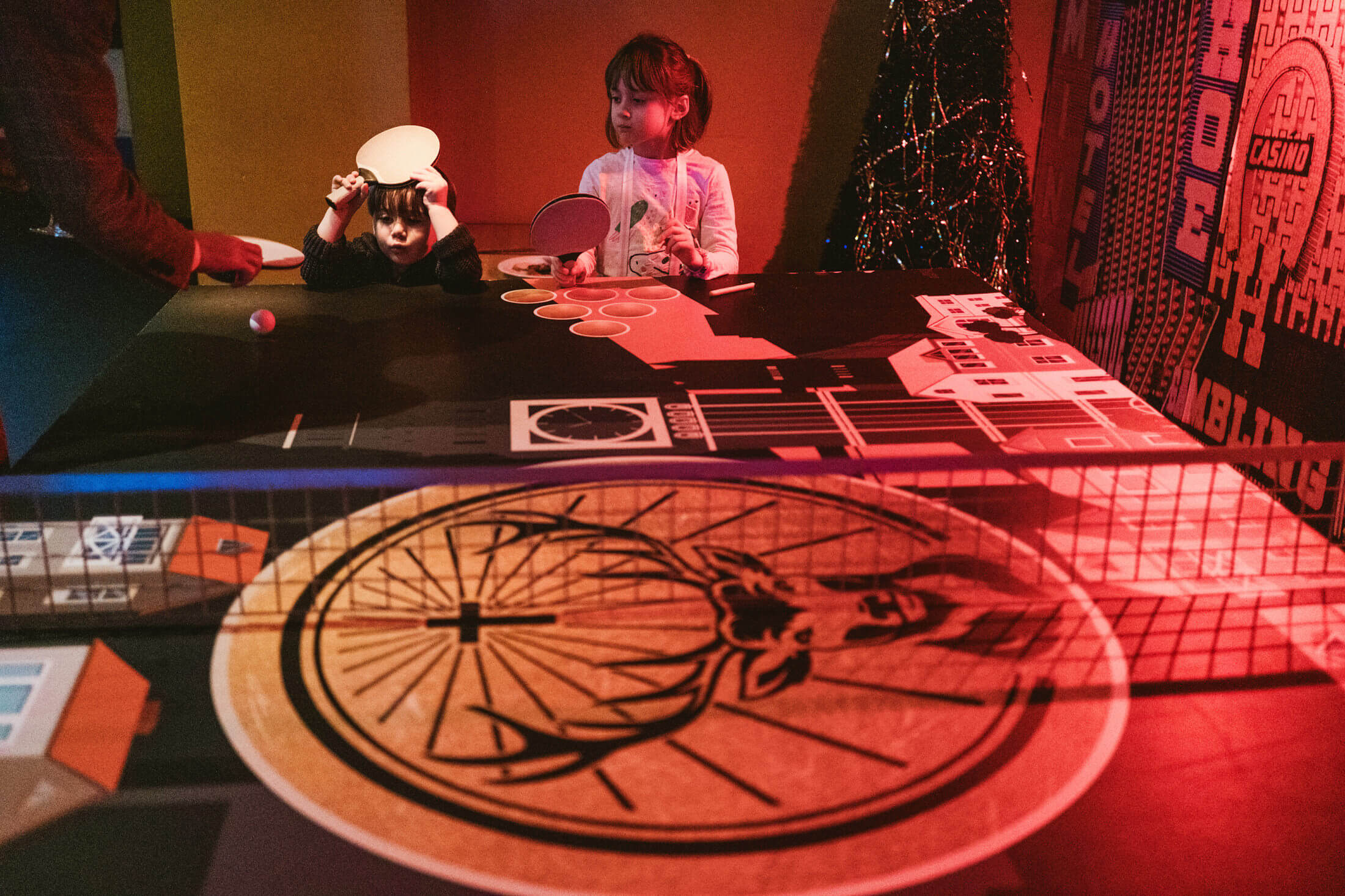 Children play table tennis under red lights at a lively wedding reception.