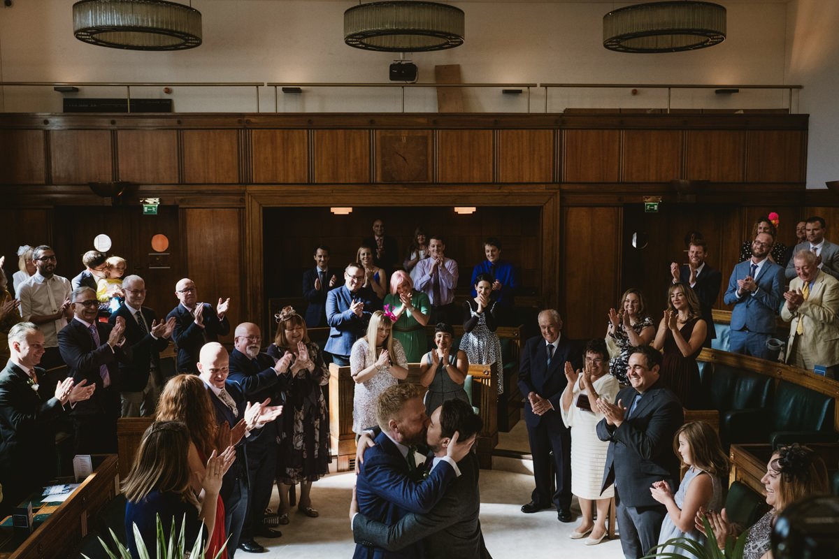 Couple kisses in court room, guests applaud.
