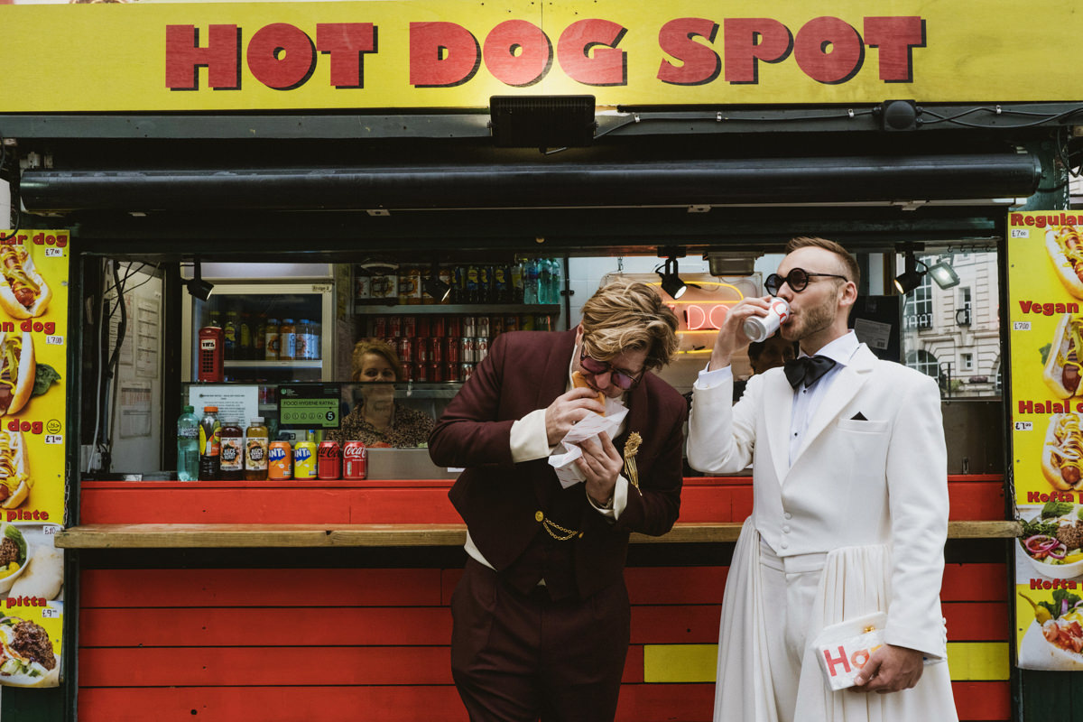 Two men eating at hot dog stand.